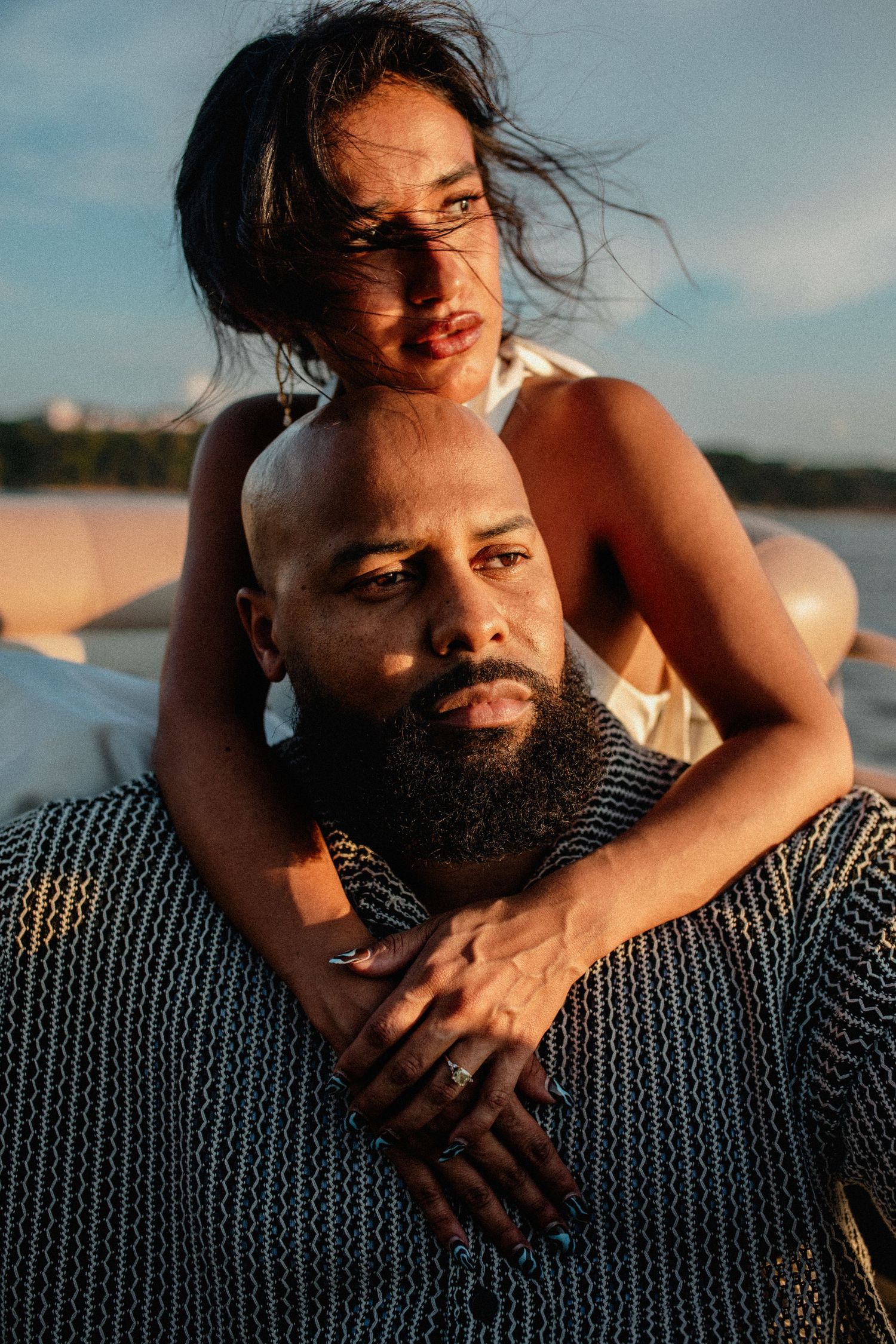 Couple embracing on a boat at sunset, woman wrapping arms around bearded mans shoulders.