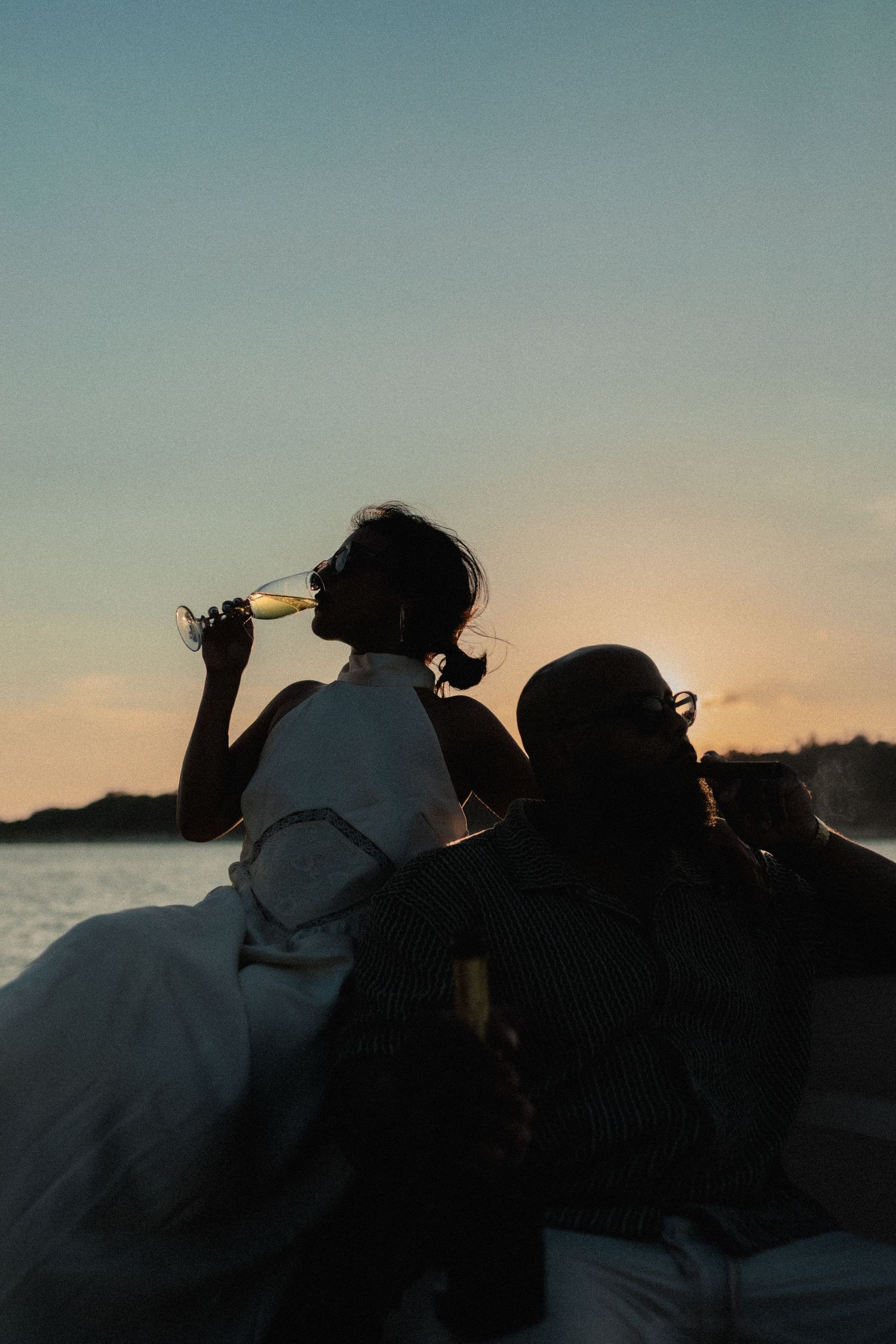 Silhouette of a couple on a boat at sunset, woman drinking champagne against colorful sky.