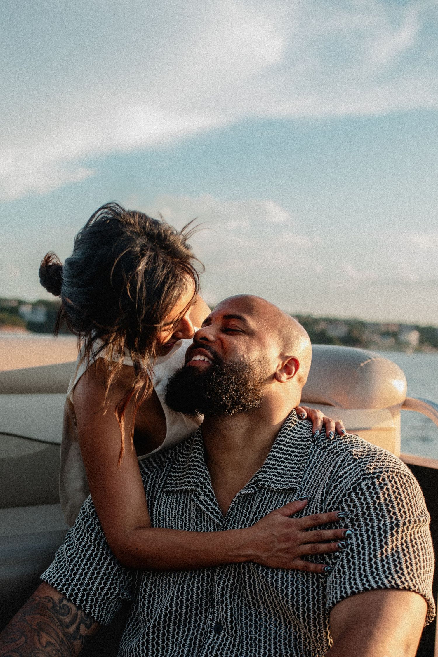 Joyful couple laughing and embracing on a boat with scenic waterfront in the background.