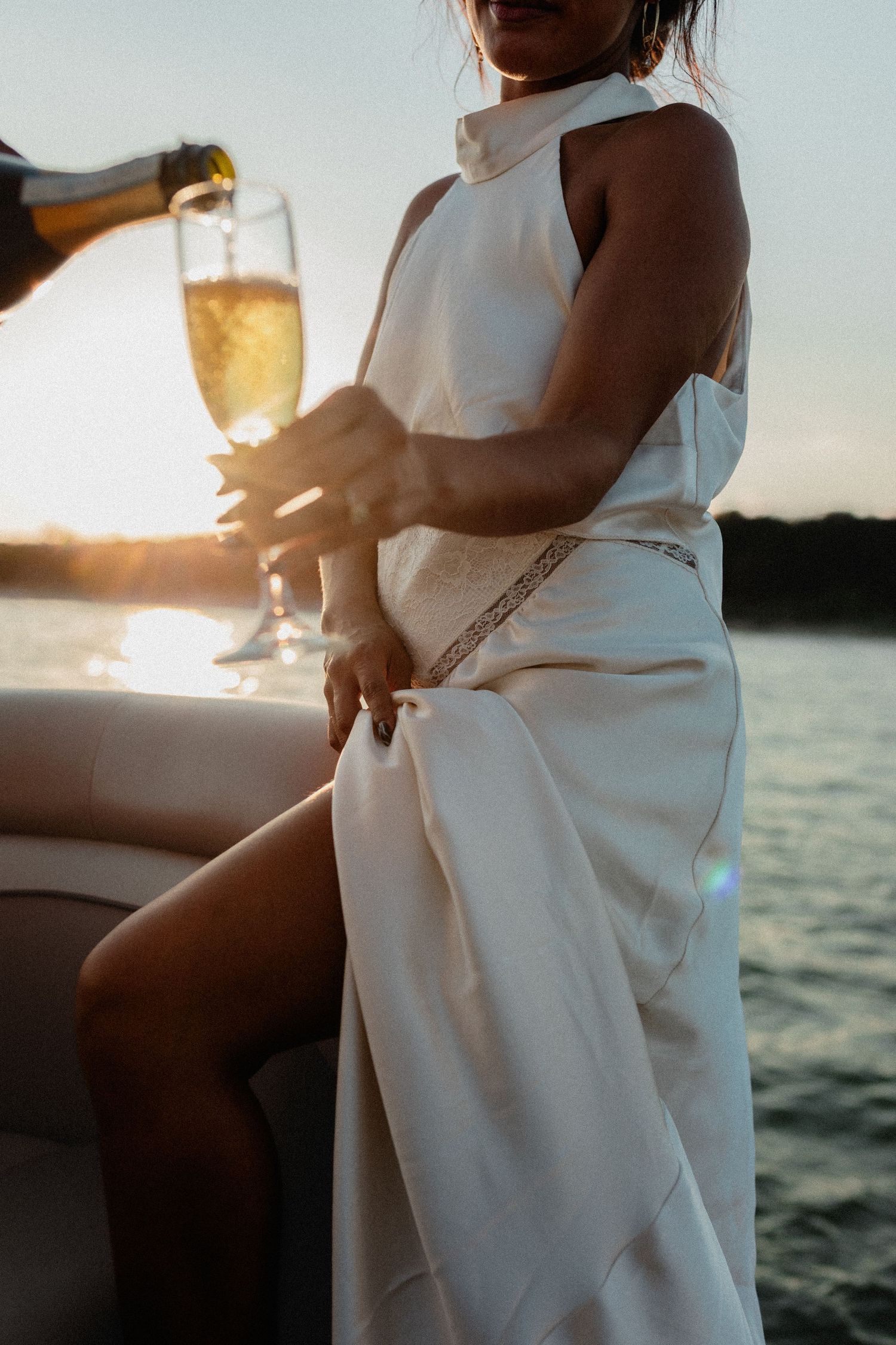 Close-up of champagne being poured into glass held by woman in elegant white dress.