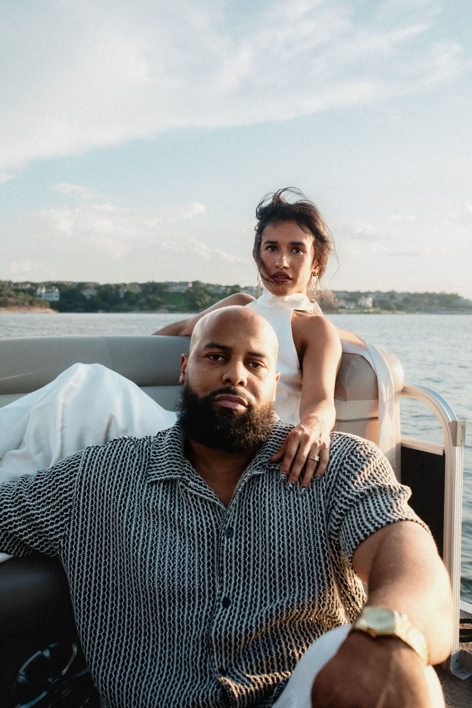 Stylish couple posing on a luxury boat, man with beard seated as woman stands behind him.
