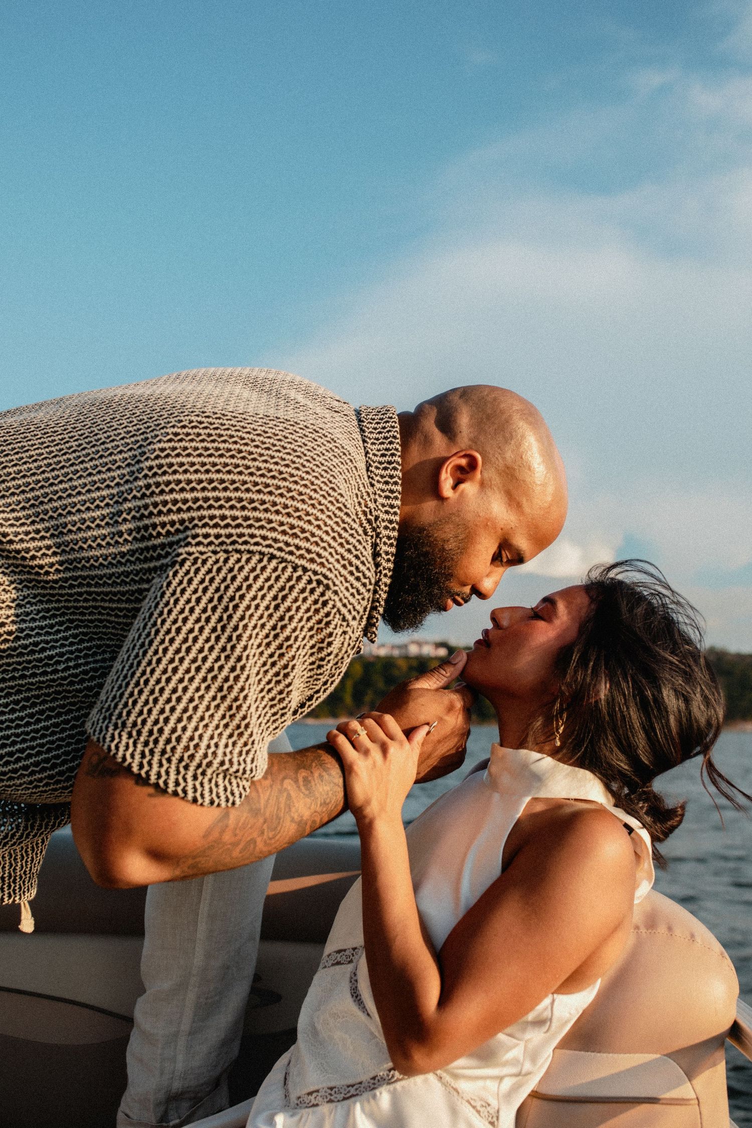 Couple leaning in for a kiss on a boat with blue sky and water in the background.