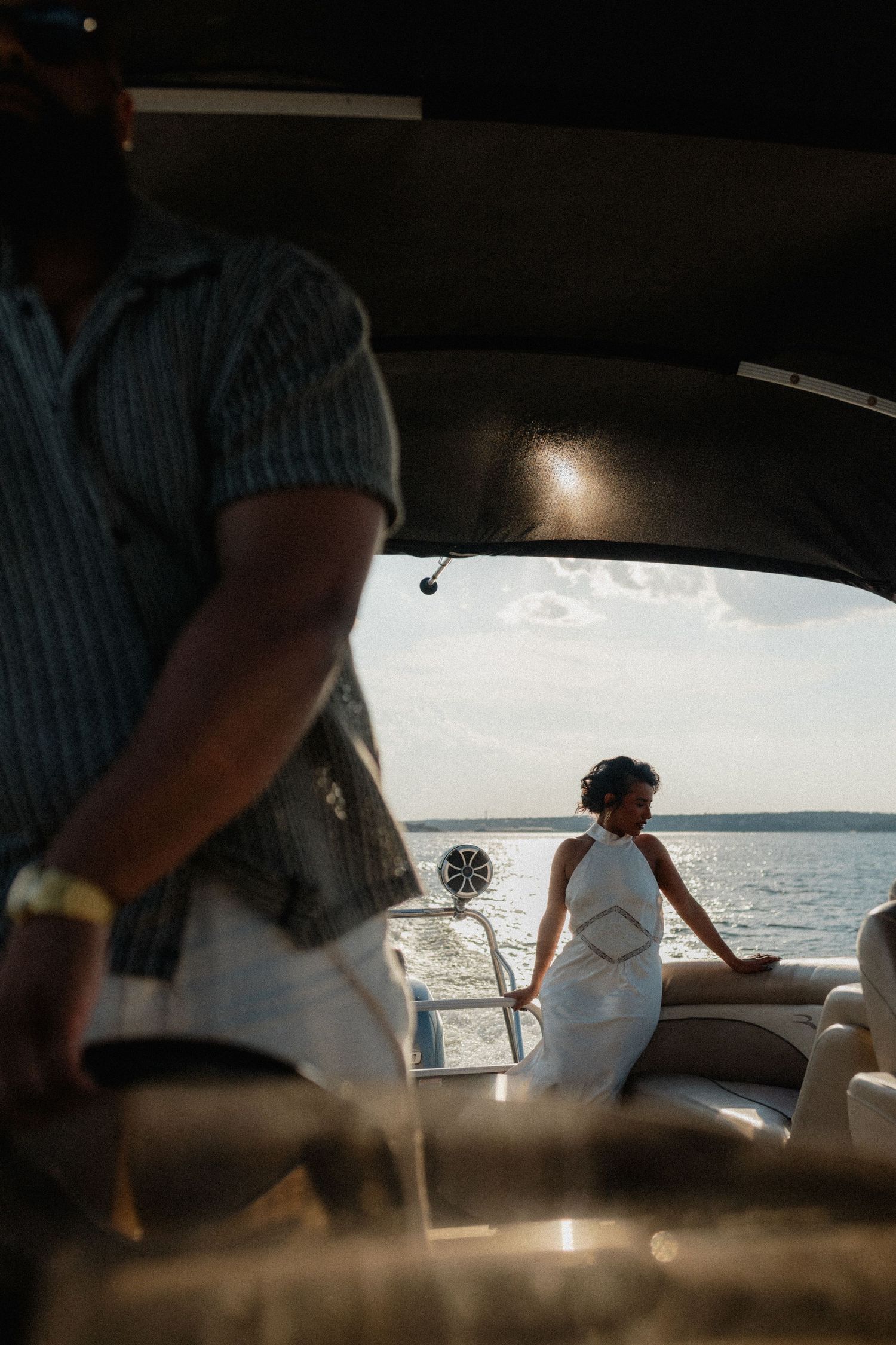 View from boat cabin of woman in white dress standing at stern overlooking open water on sunny day.