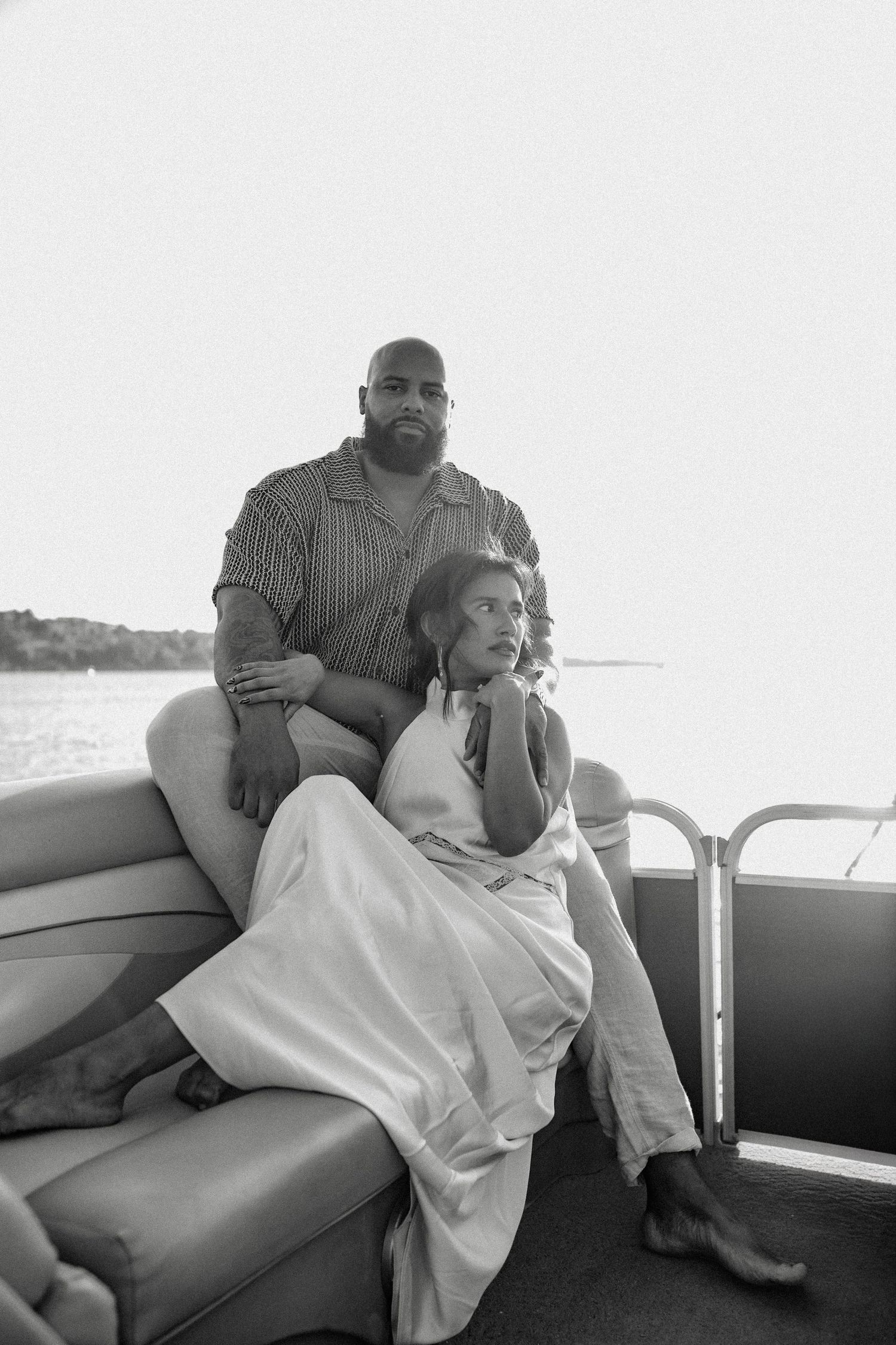 Black and white photo of a couple sitting together on a pontoon boat on the water.