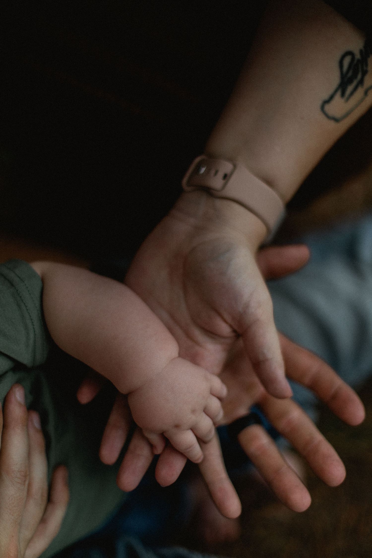 Close-up of parents hands cradling tiny baby feet, mother with wrist tattoo visible.