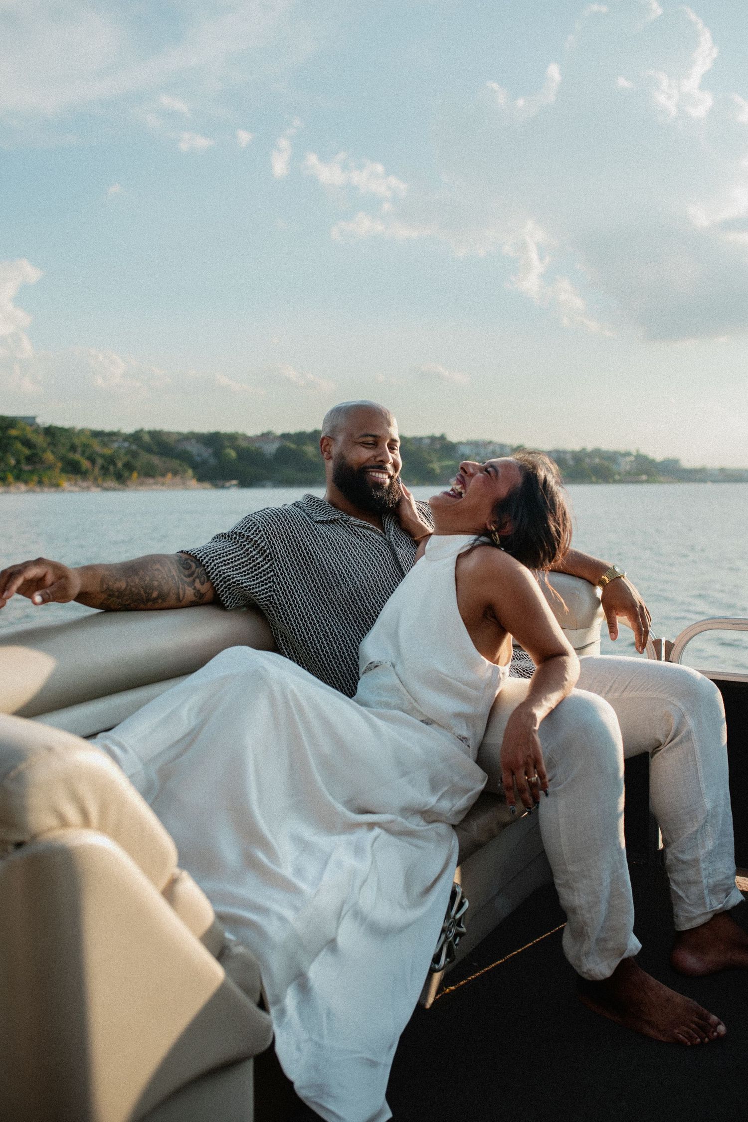 Joyful couple lounging on a boat, woman laughing with head back, man smiling beside her on the water.