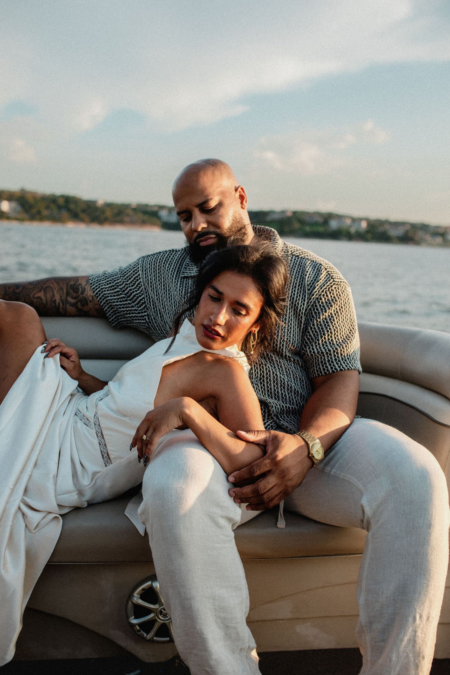 Couple cuddling on a luxury boat at sunset with serene waterfront scenery behind them.