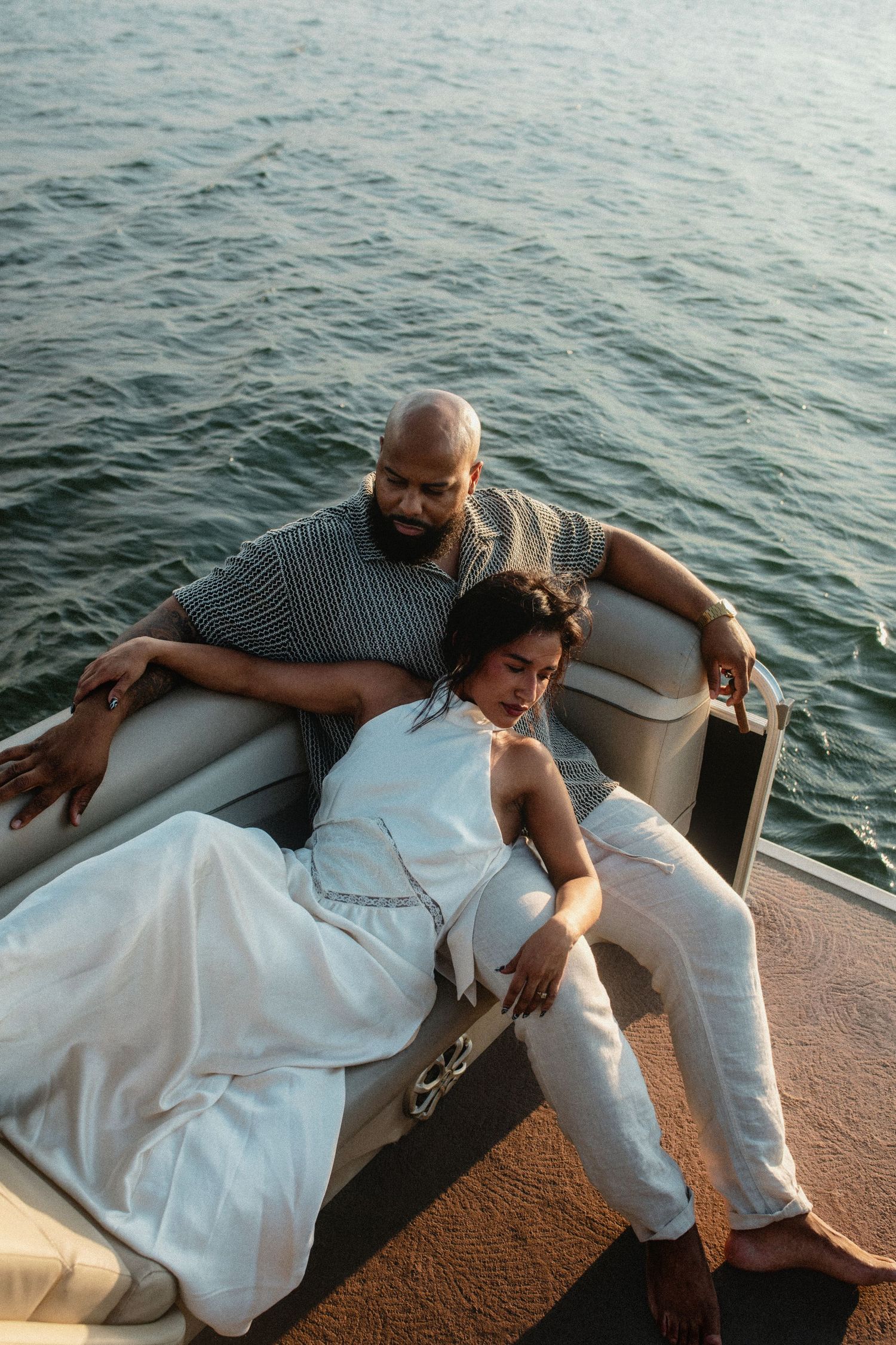 Couple relaxing together on a pontoon boat, woman in white dress leaning on mans chest.