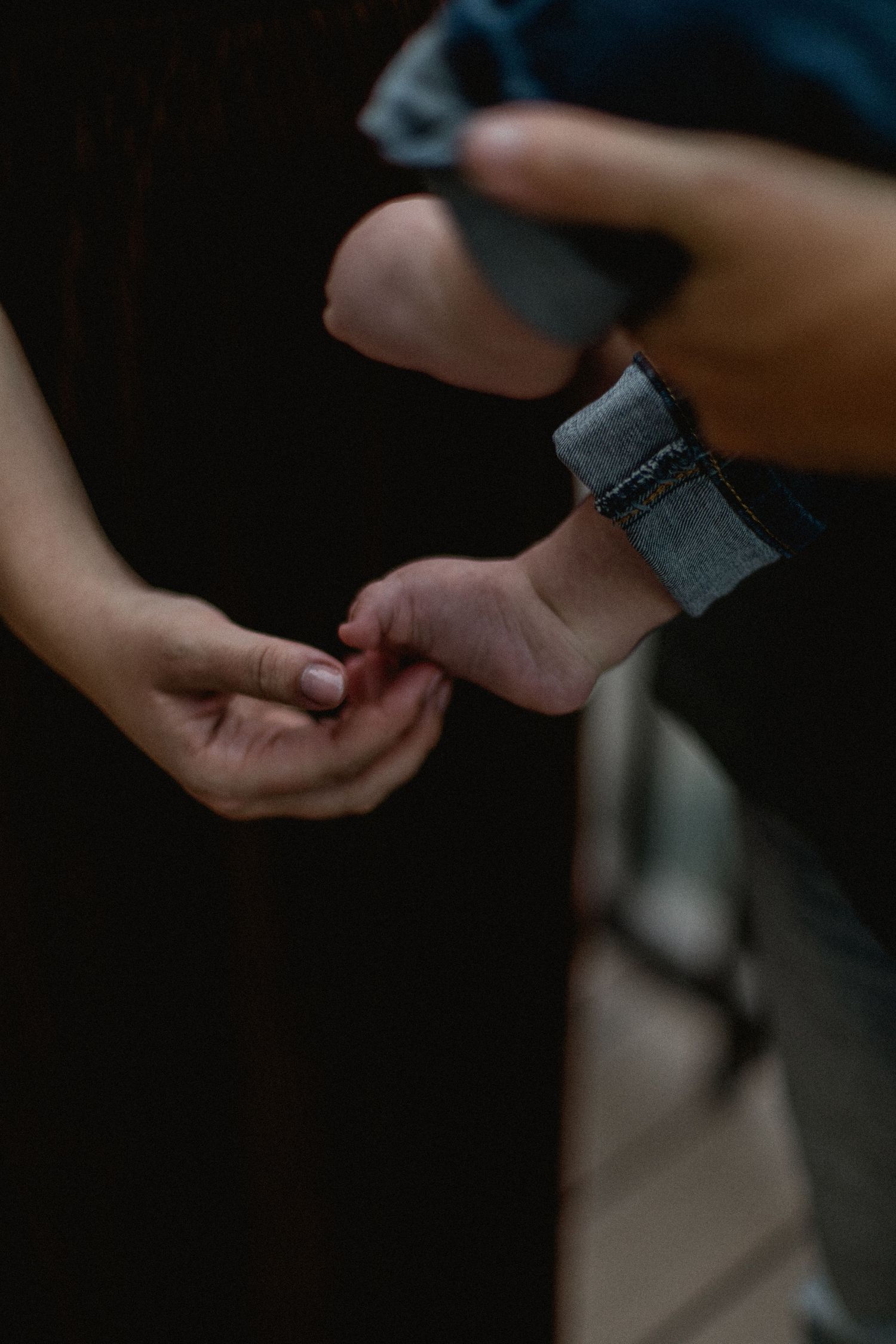 Gentle close-up of parents holding their babys tiny foot in dark, intimate setting.