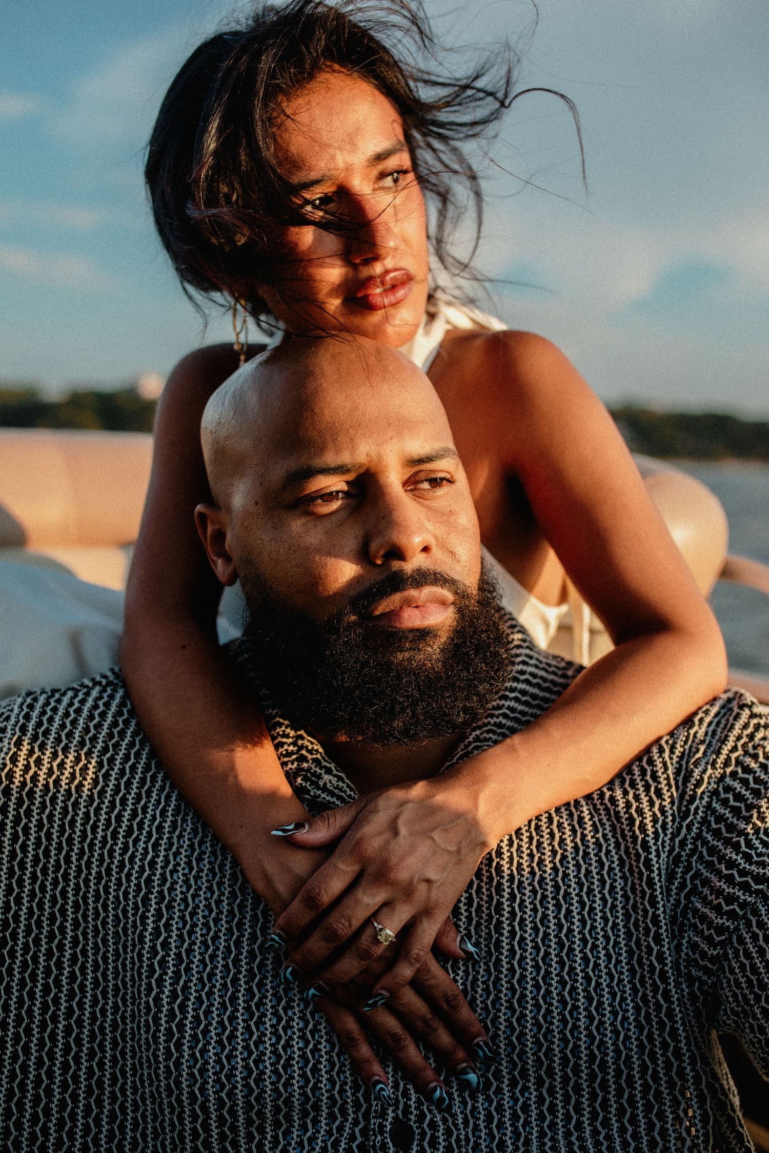 Intimate couple portrait on a boat, woman embracing bald bearded man in warm golden light.