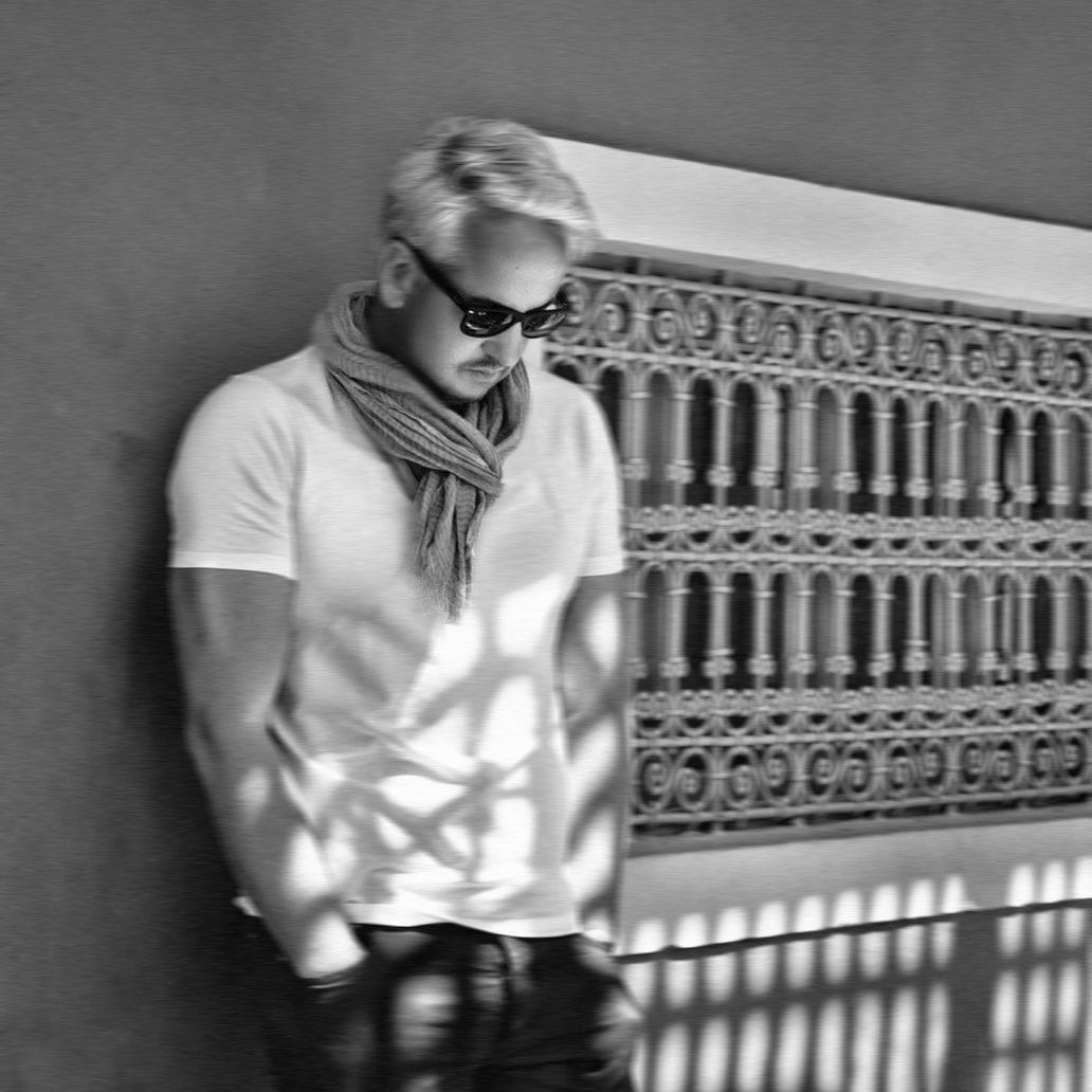 Photo en noir et blanc d'un homme élégant en lunettes de soleil et en écharpe se penchant contre un mur de clôture en fer décoratif.