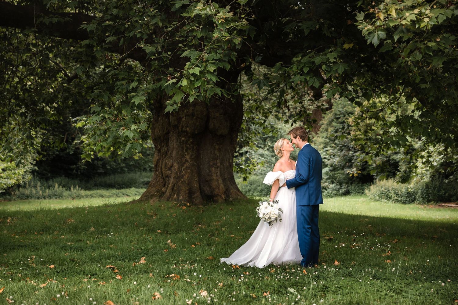 La mariée et le marié partagent un baiser sous un grand arbre dans un jardin ensoleillé le jour de leur mariage.