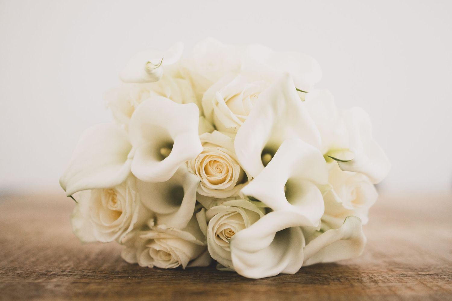 Élégant bouquet de mariée de lys calla blancs et de roses crème sur une surface en bois.