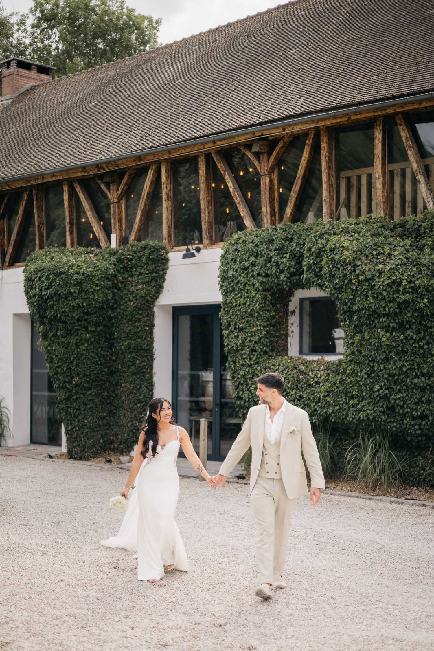 La mariée et le marié marchent main dans la main à l'extérieur du lieu de mariage rustique.