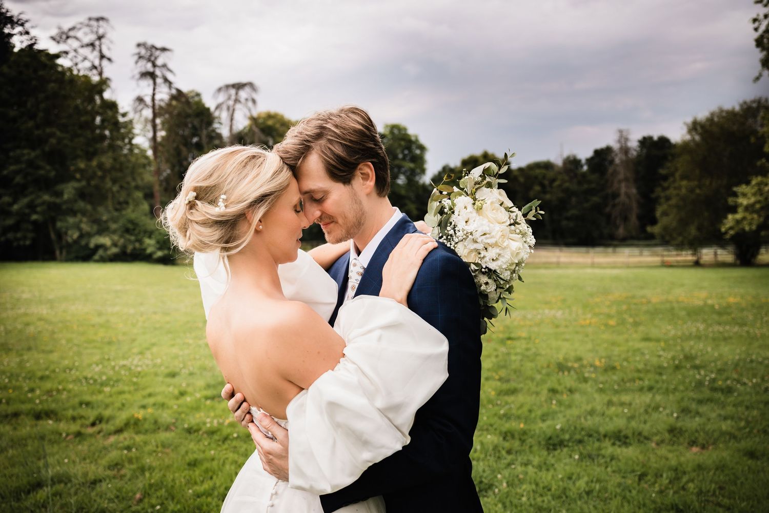 La mariée et le marié s'embrassent intimement sur un gazon vert luxuriant le jour de leur mariage.