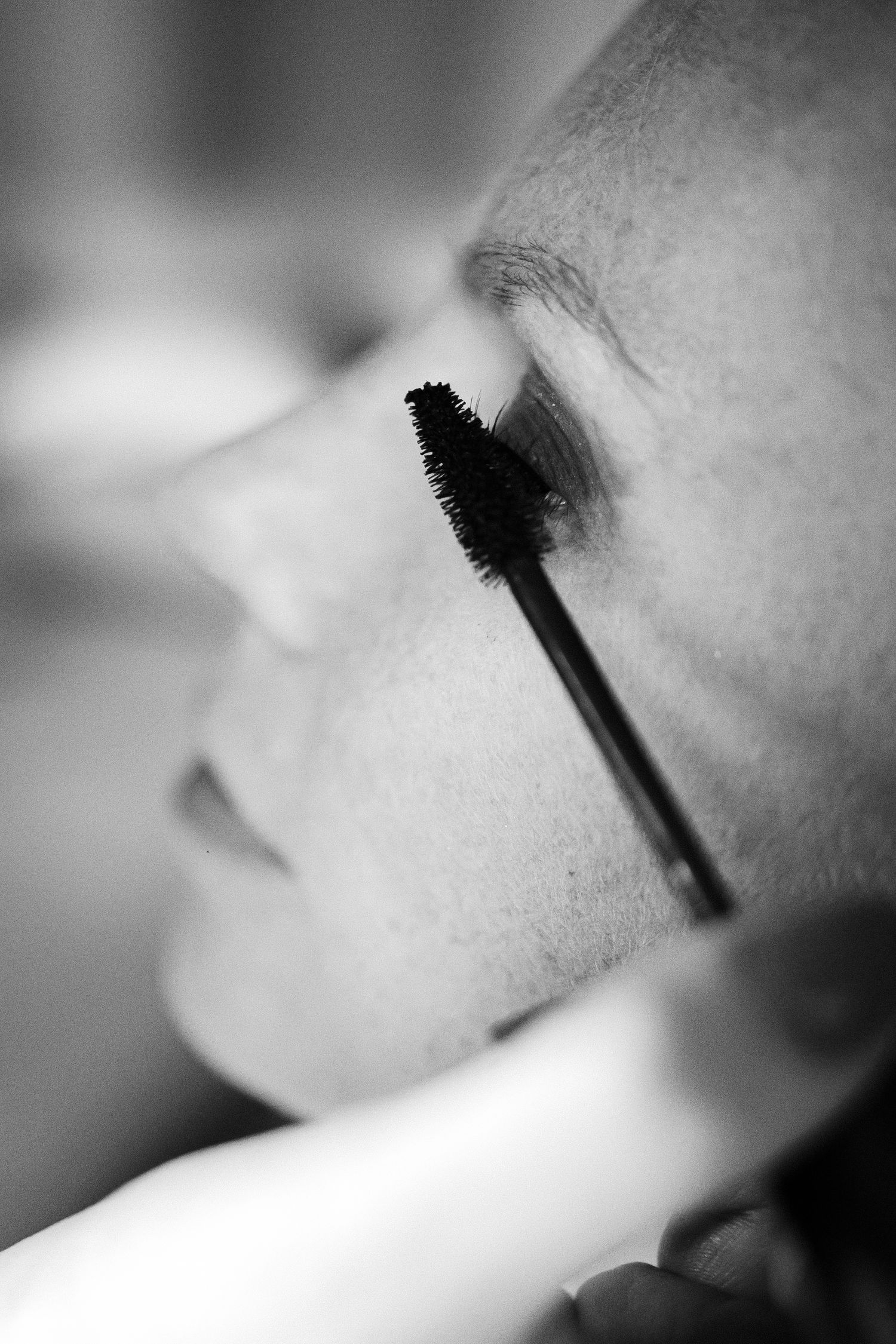 Photo en noir et blanc en gros plan d'une mariée ayant du mascara appliqué sur ses cils pendant les préparatifs du mariage.