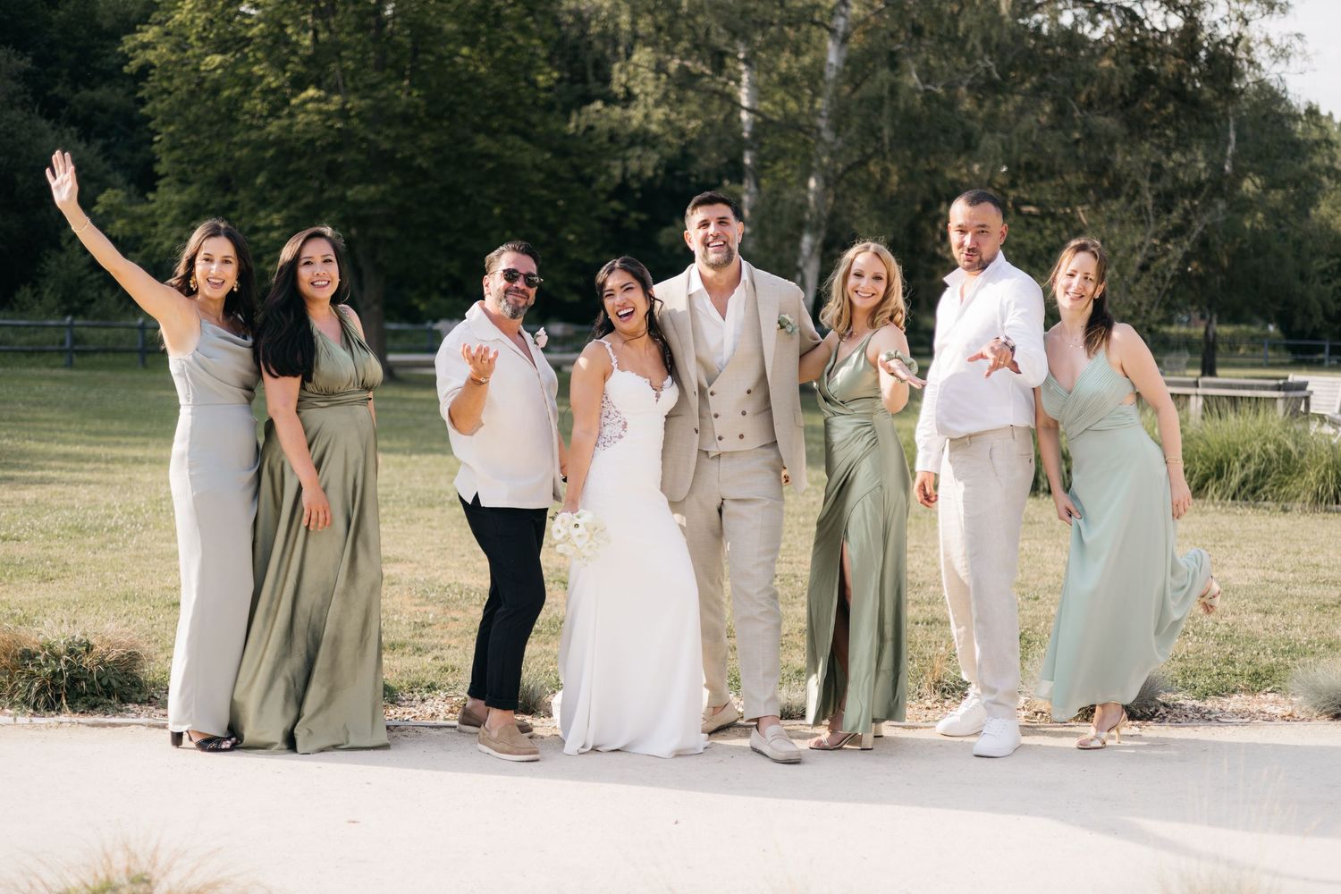 La fête de mariage pose à l'extérieur dans des robes de demoiselle d'honneur vert sauge avec la mariée et le marié au centre.