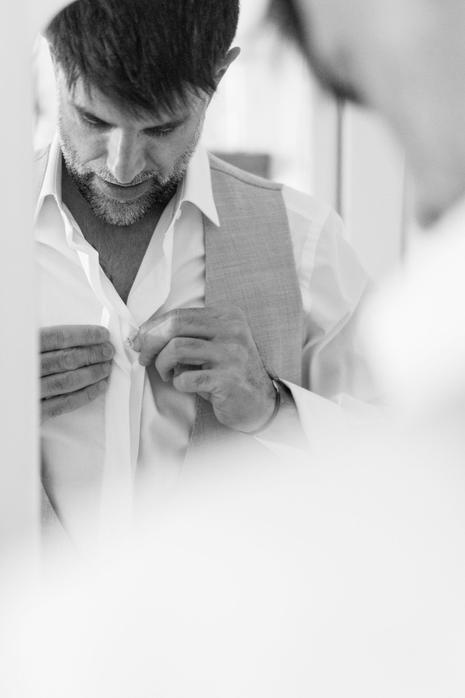 Photo en noir et blanc du marié boutonné sa chemise en se préparant pour son jour de mariage.