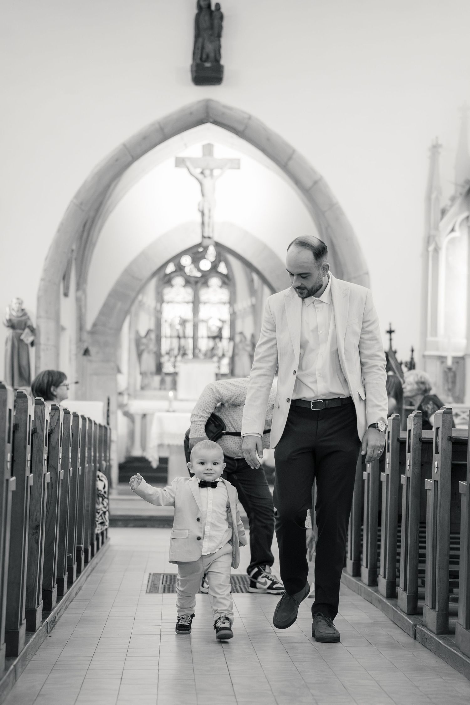 Parrain et enfant remontant l'allée centrale de l'église, photographie noir et blanc — photographe baptême Luxembourg