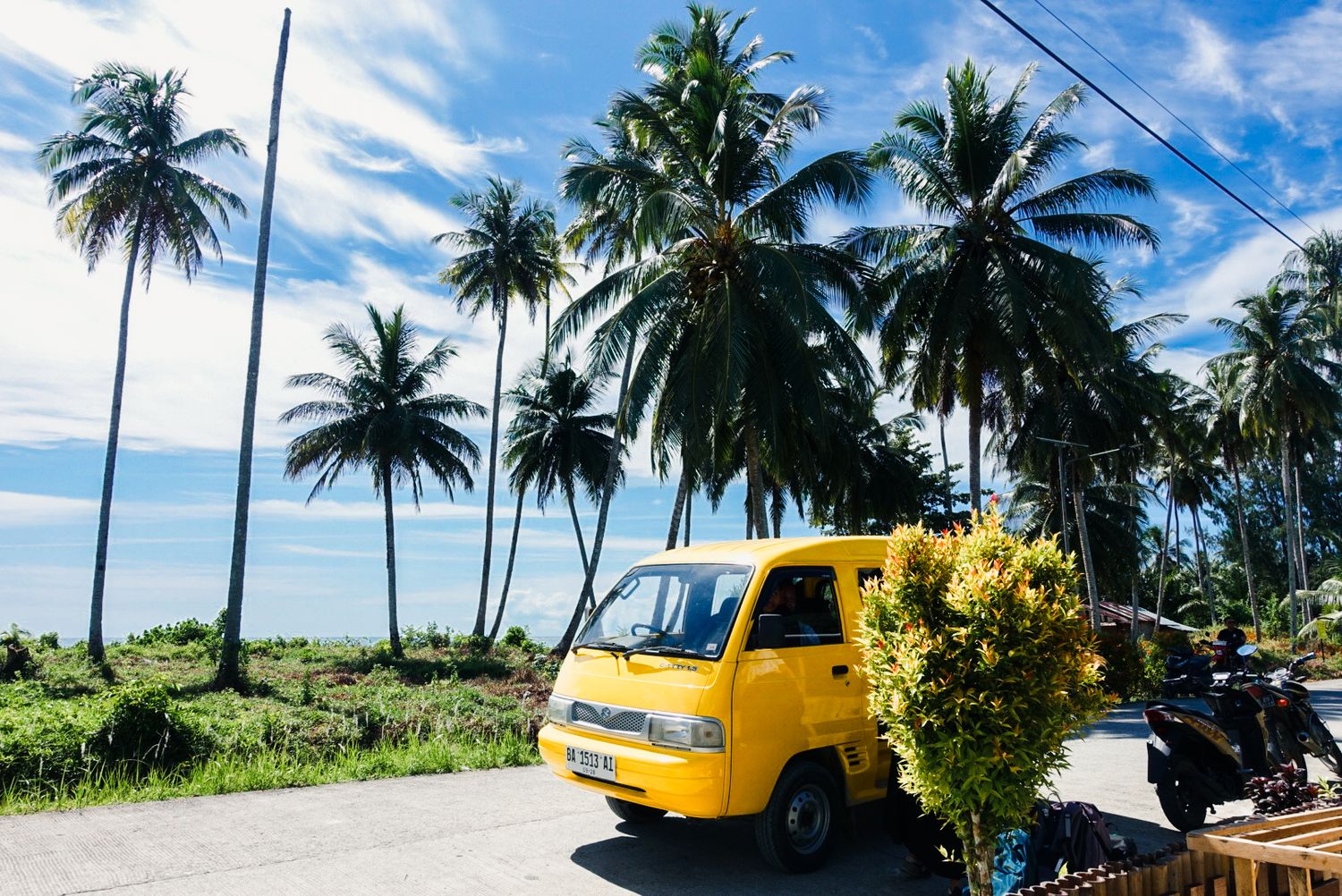 Camionnette jaune sur une route bordée de cocotiers face à l'océan — îles Mentawaï, Indonésie
