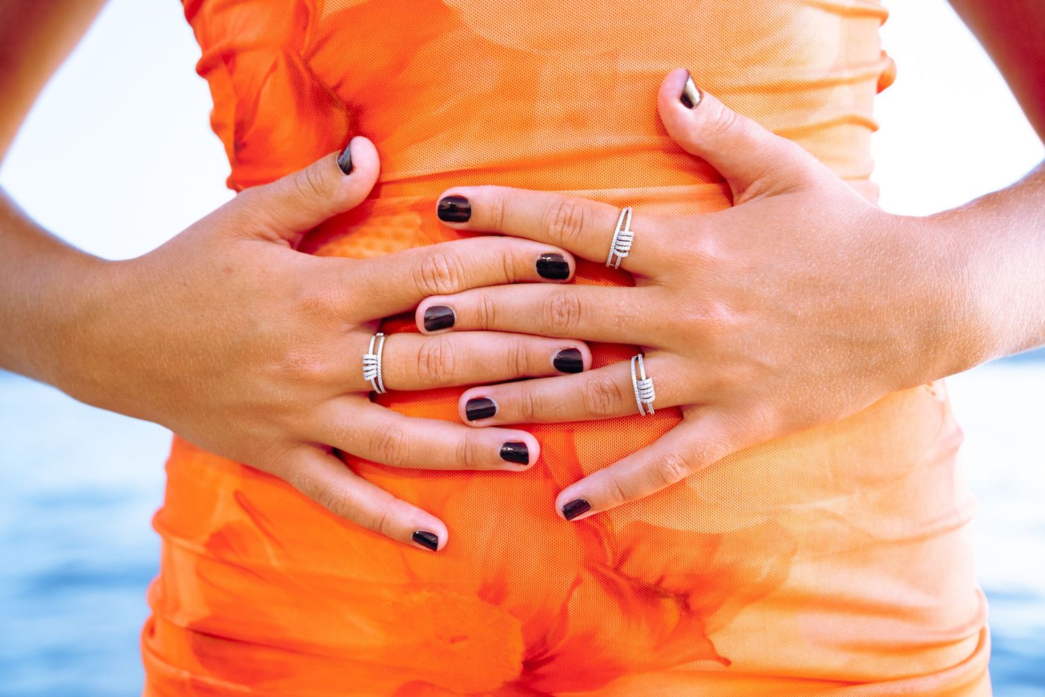Mains portant plusieurs bagues fines posées sur une combinaison orange — photographie de bijoux en lifestyle