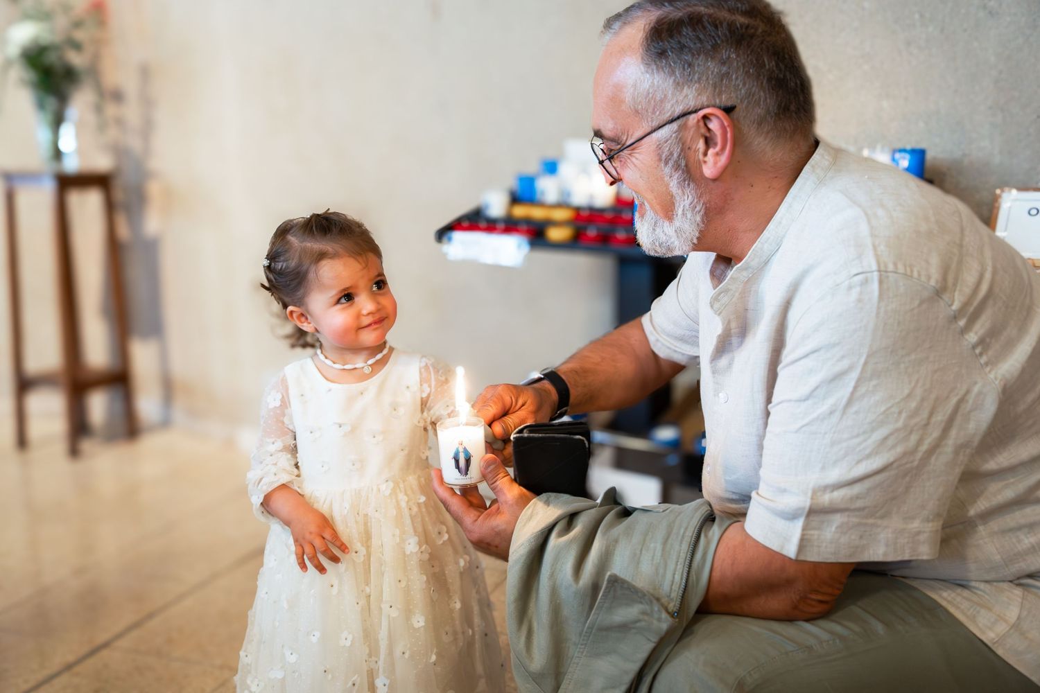 Grand-père allumant le cierge de baptême avec l'enfant dans l'église — photographe baptême Luxembourg