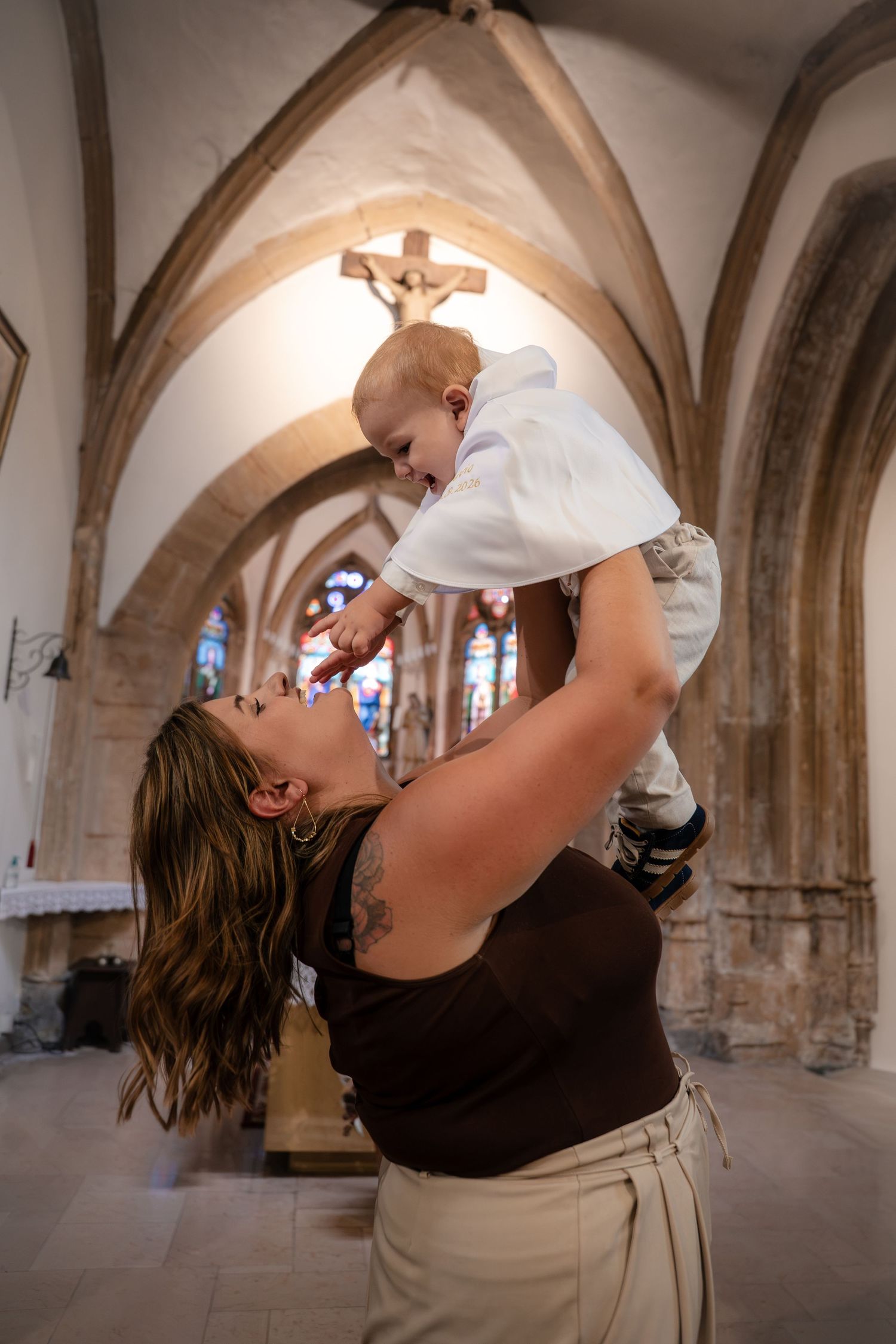 Mère soulevant son bébé dans ses bras sous les voûtes de l'église — photographe baptême Luxembourg
