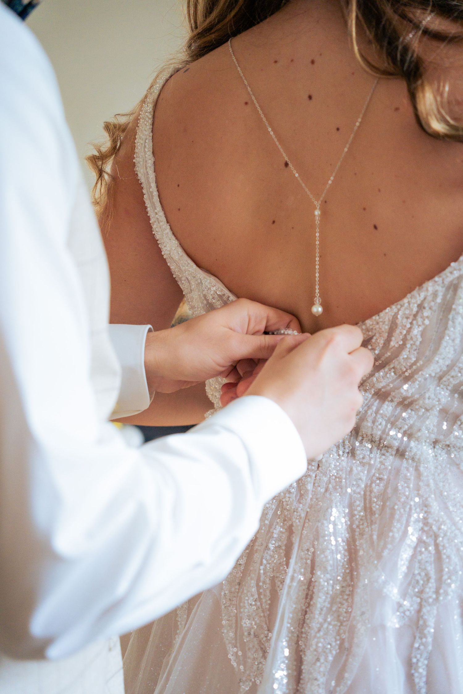 Boutonnage de la robe de mariée pailletée, bijou de dos en perles – détail des préparatifs de mariage