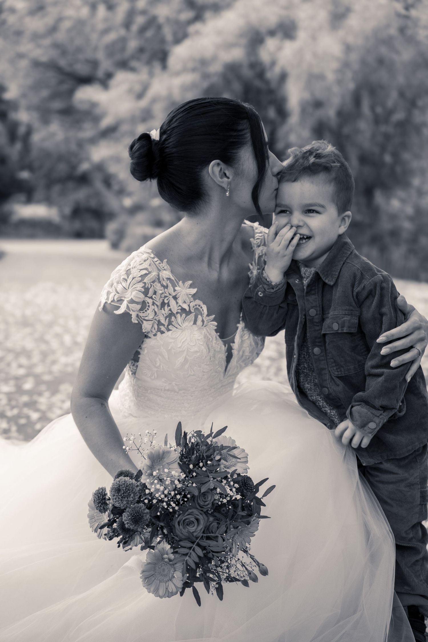 Mariée souriante avec un petit garçon dans les bras, bouquet de fleurs, portrait en noir et blanc – photographe de mariage en Lorraine