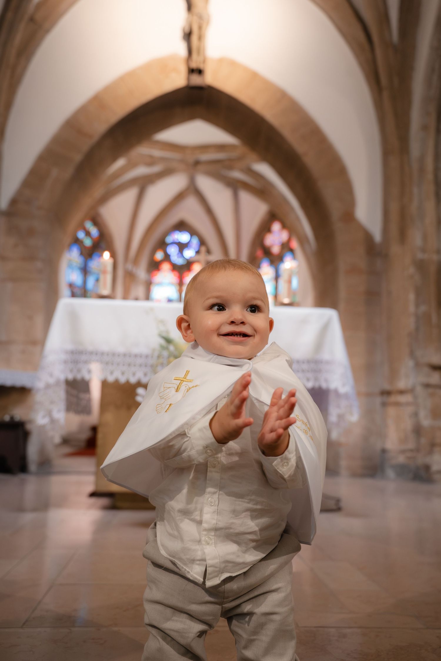 Jeune enfant souriant devant l'autel, vêtu de sa tenue de baptême — photographe baptême Luxembourg