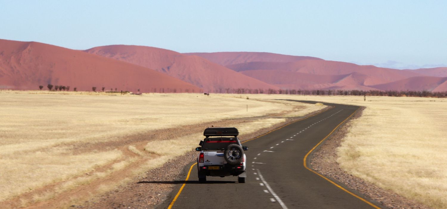 4x4 avec tente de toit sur une route du désert namibien, dunes rouges à l'horizon – photographe de voyage en Namibie