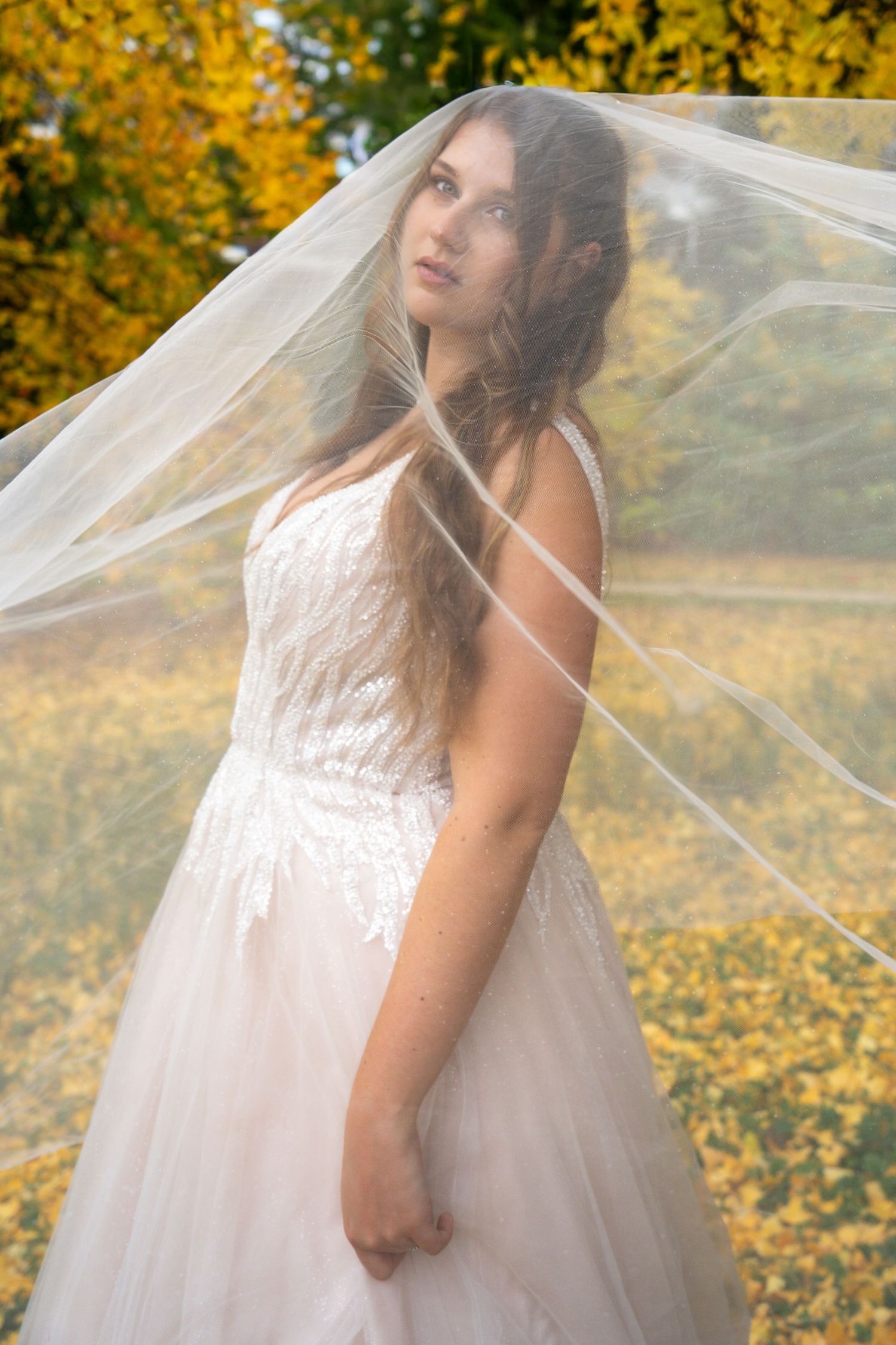 Mariée sous son voile dans un parc aux couleurs d'automne, feuillage jaune – séance photo de mariage en Moselle