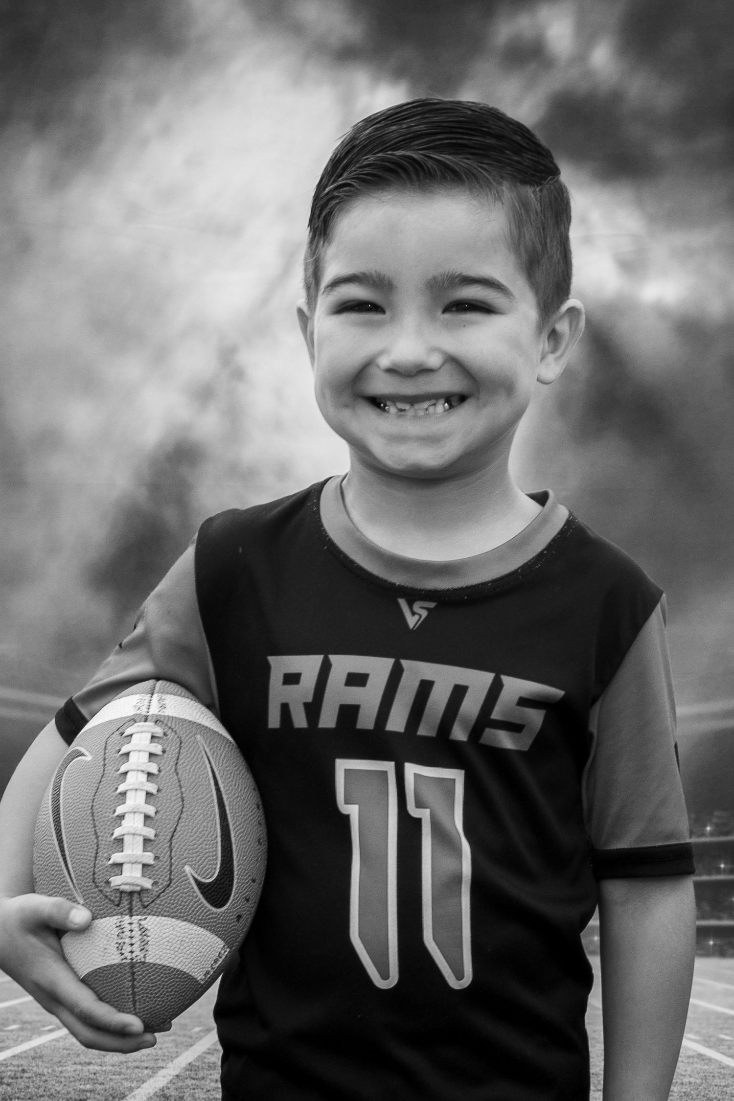 Young boy wearing a Rams football jersey holding a football in a portrait session by Tiny Toes to Tassels Photography in Springtown, TX