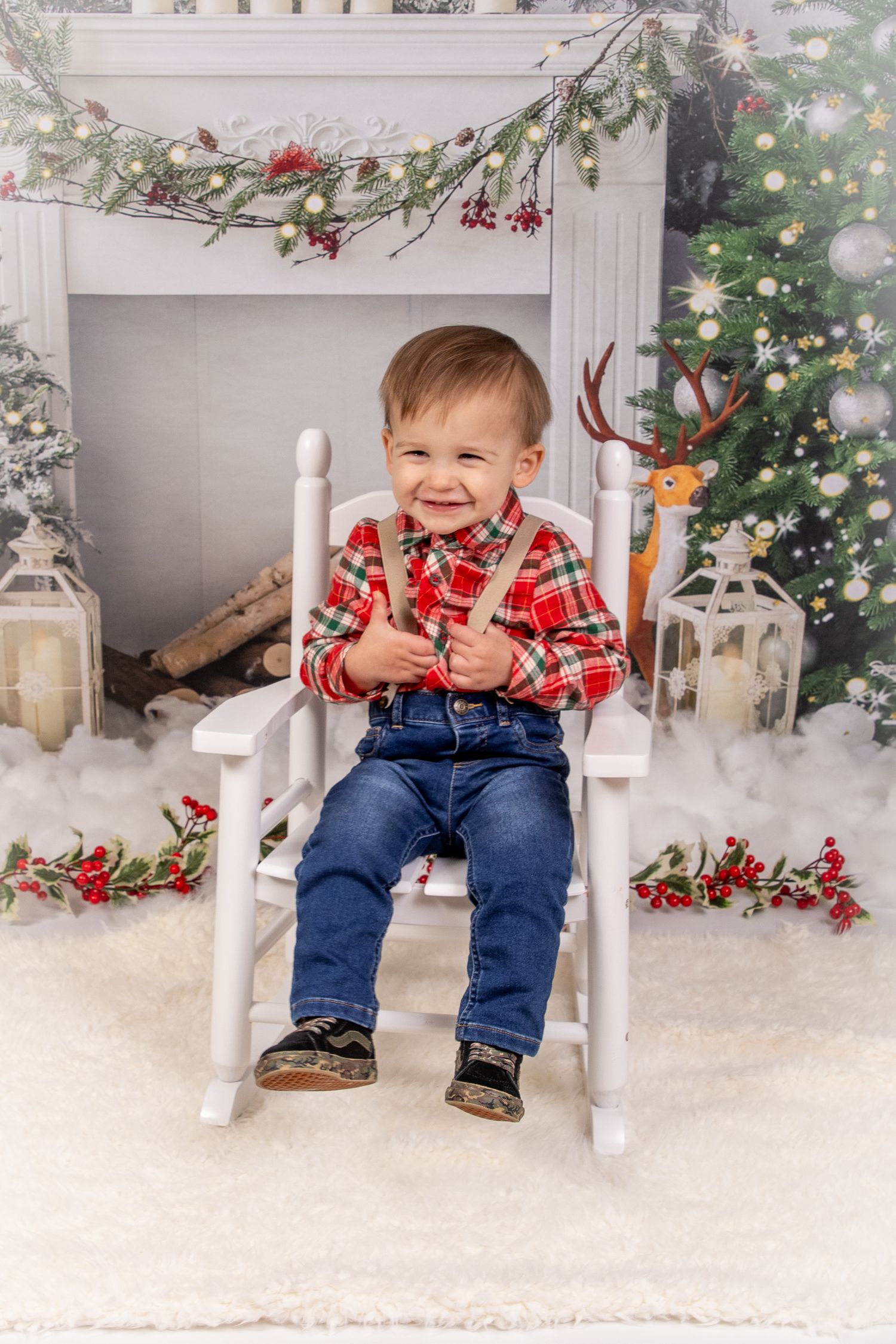 Toddler boy wearing a red plaid shirt, denim, and red suspenders sitting in a white rocking chair by a holiday tree in Springtown, TX