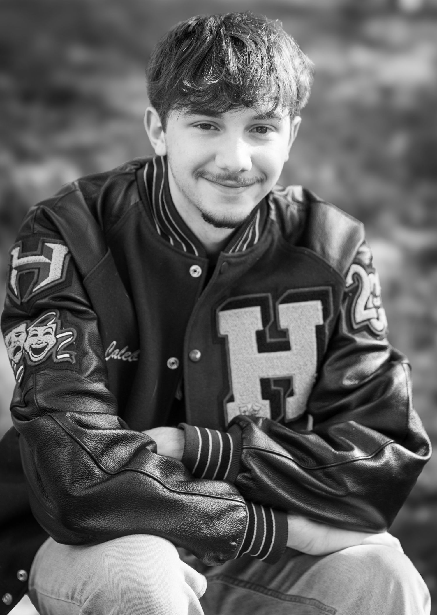 High school senior boy wearing a letterman jacket outdoors during a portrait session by Tiny Toes to Tassels Photography