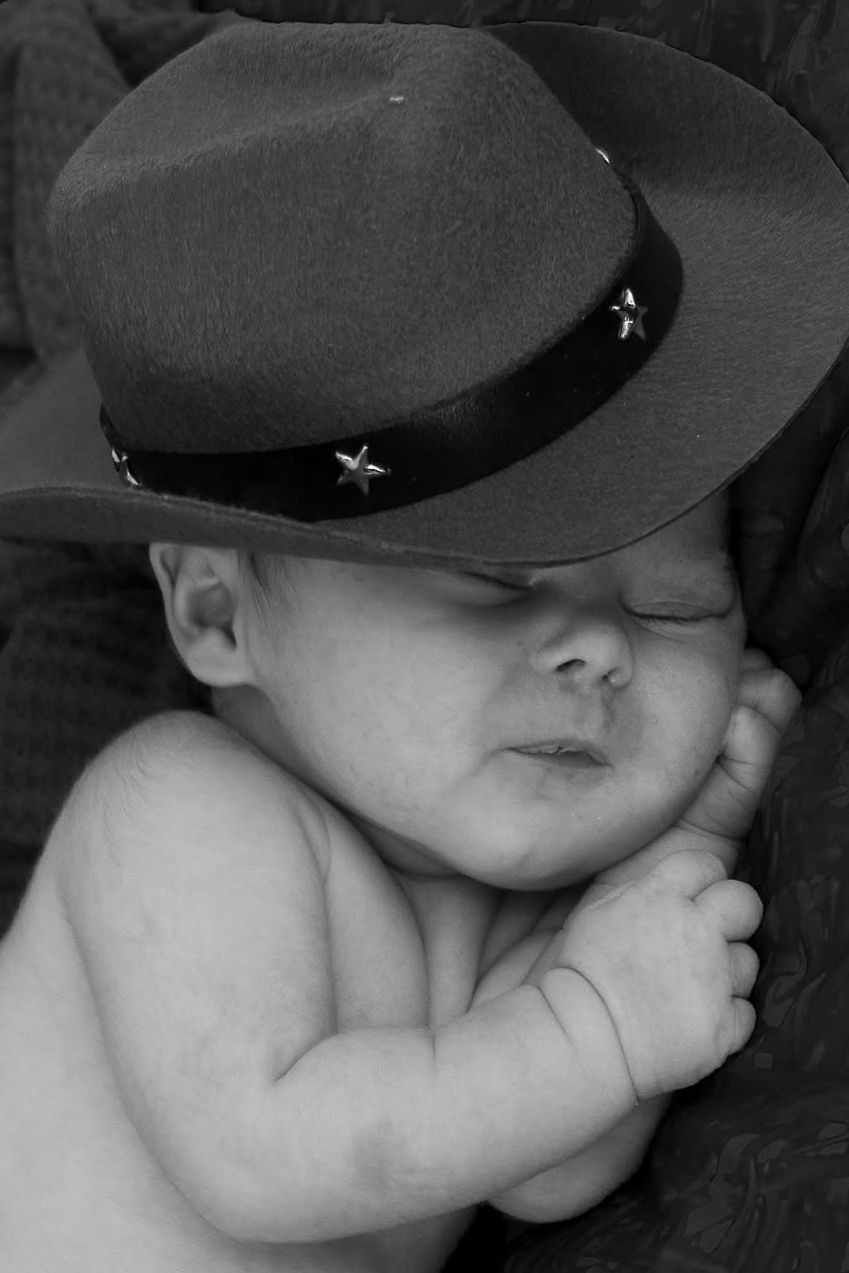 Newborn baby wearing a tiny hat and resting peacefully by Tiny Toes to Tassels Photography in Springtown, TX