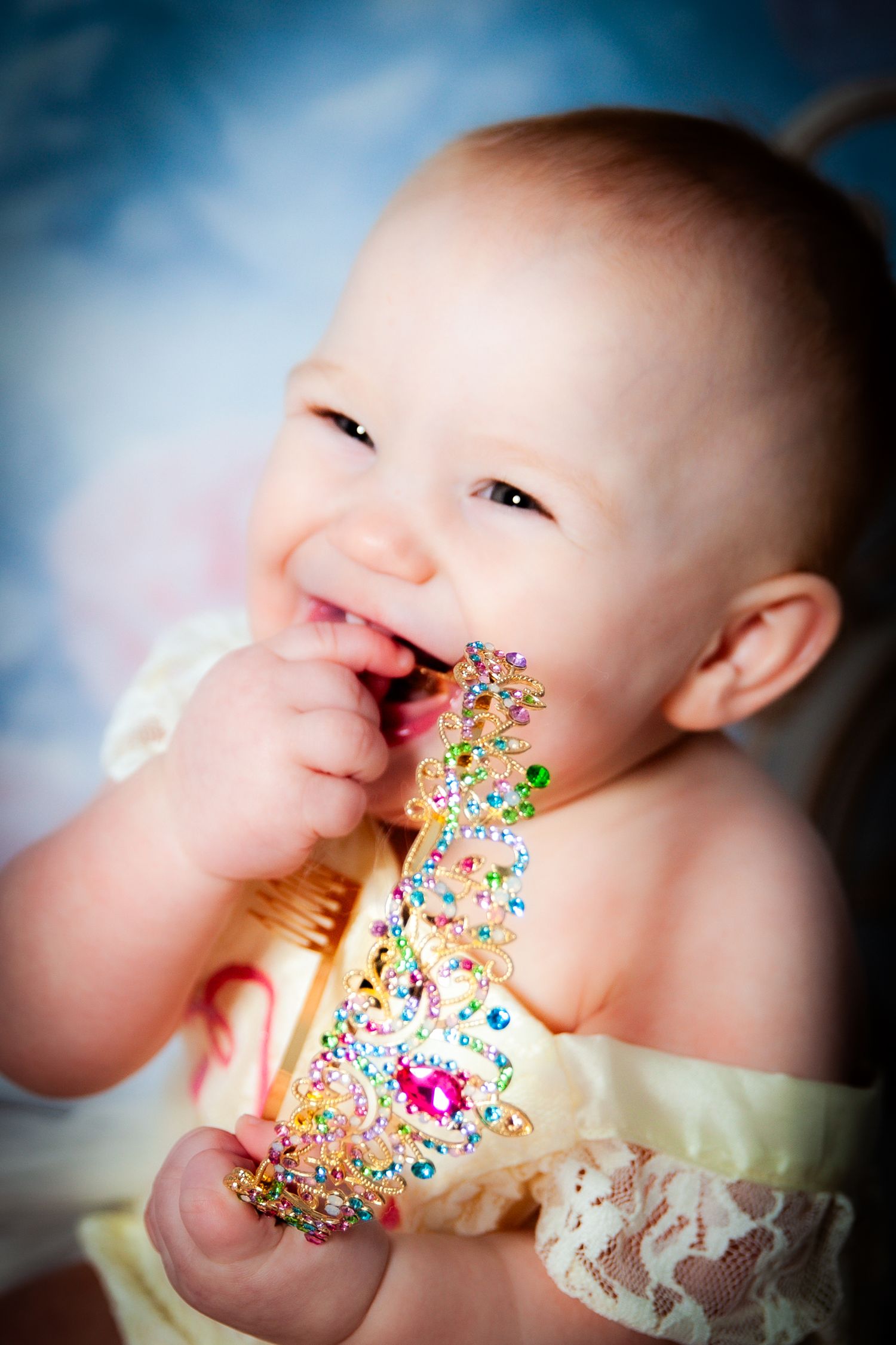 Baby girl smiling and holding a colorful toy rattle during a milestone portrait session by Tiny Toes to Tassels Photography