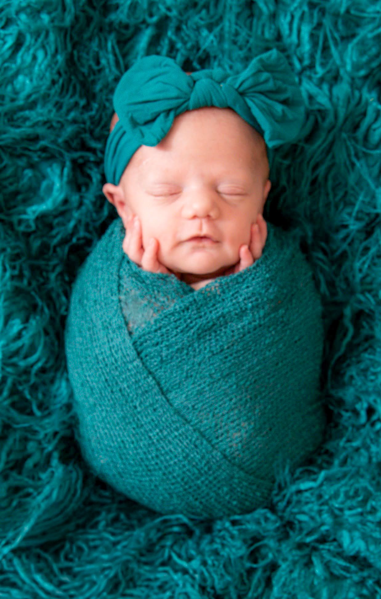 Newborn baby wrapped in vibrant teal with matching floral headband by Tiny Toes to Tassels Photography in Springtown, TX