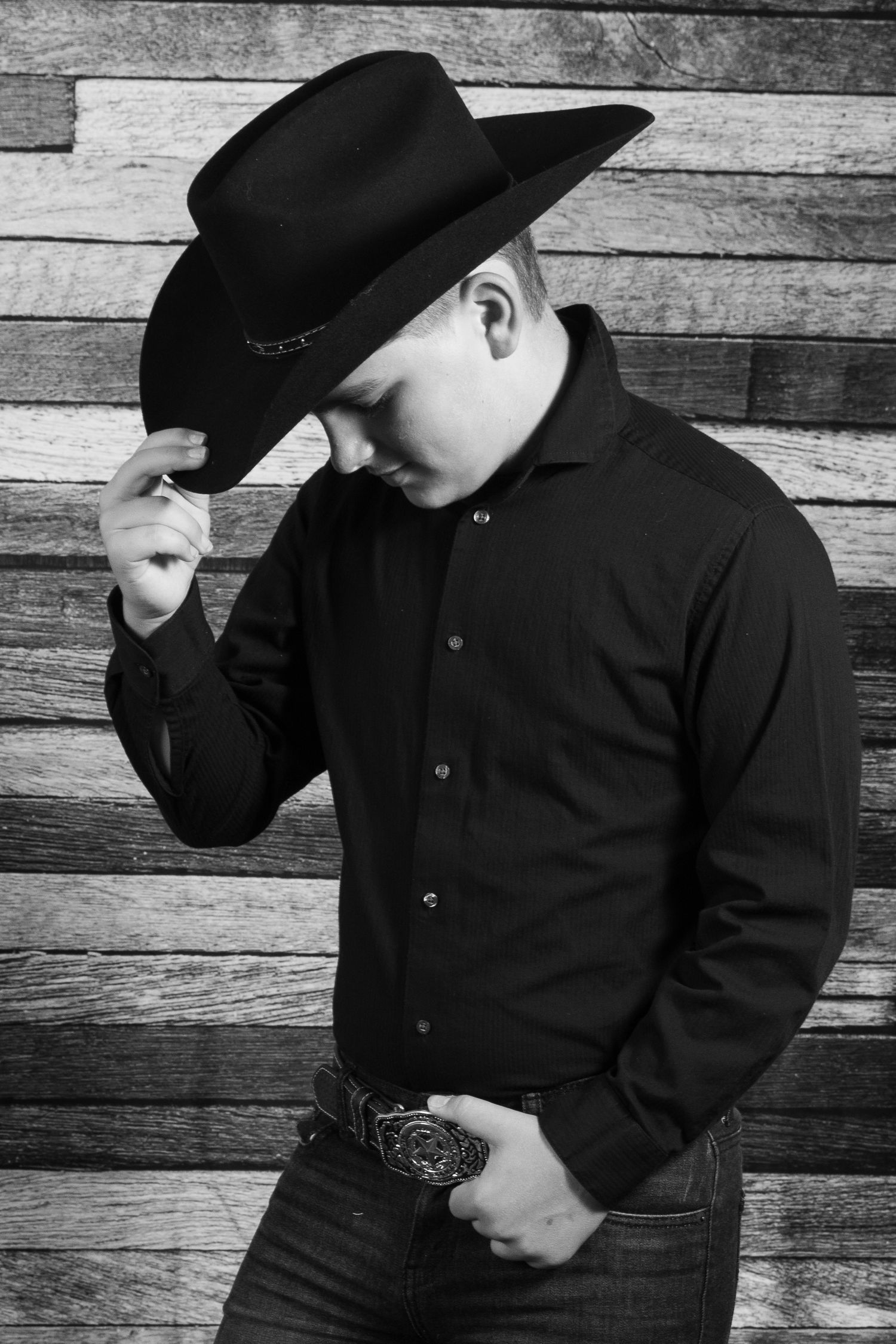 Young boy wearing a black shirt and a cowboy hat during a portrait session by Tiny Toes to Tassels Photography in Springtown, TX