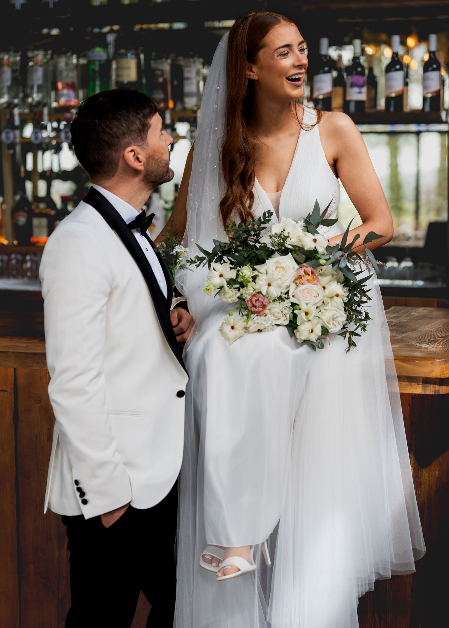 Bride laughing with the groom while holding her bouquet at the wedding venue bar.
