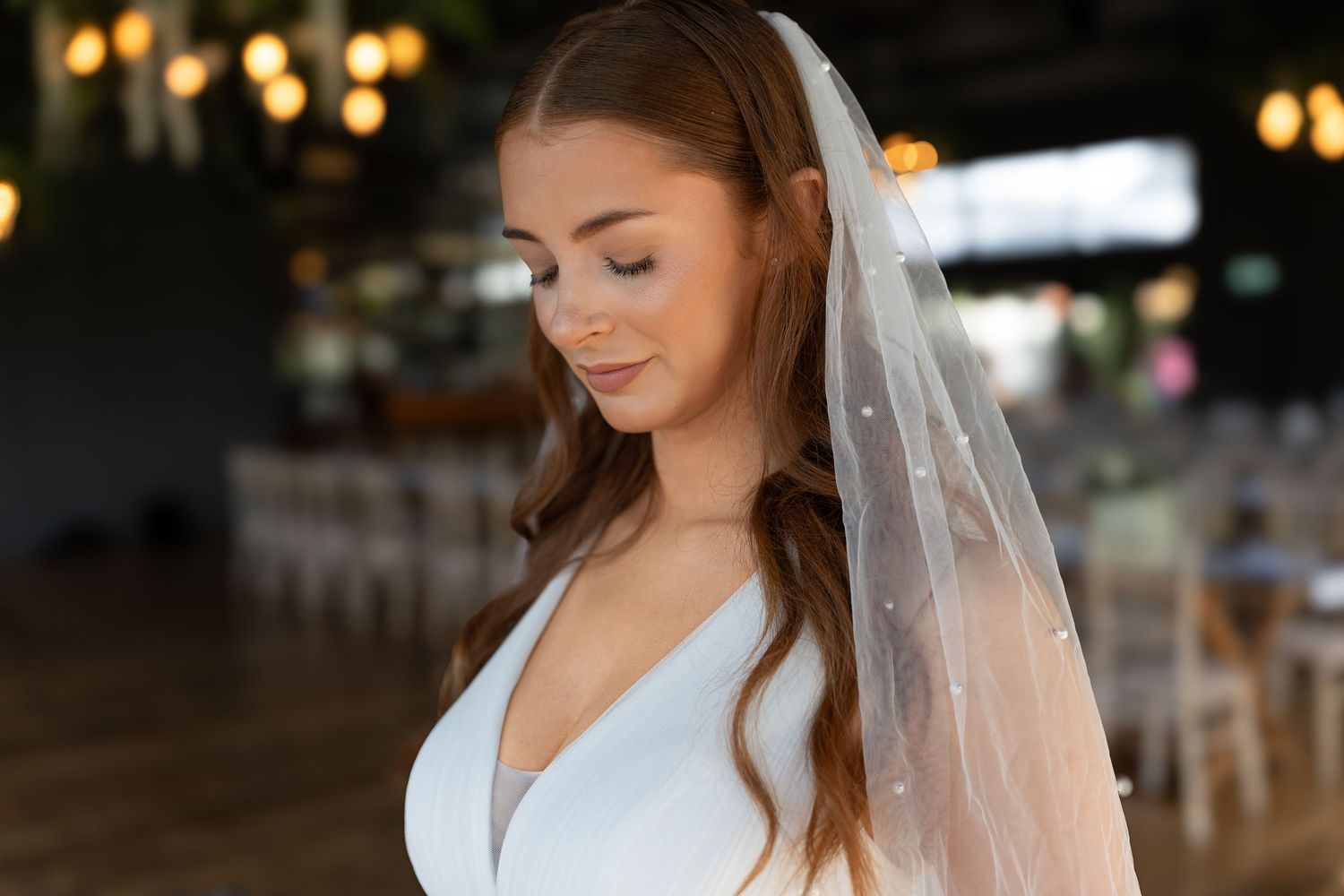 Elegant bridal portrait with a soft veil and warm lights glowing in the wedding venue