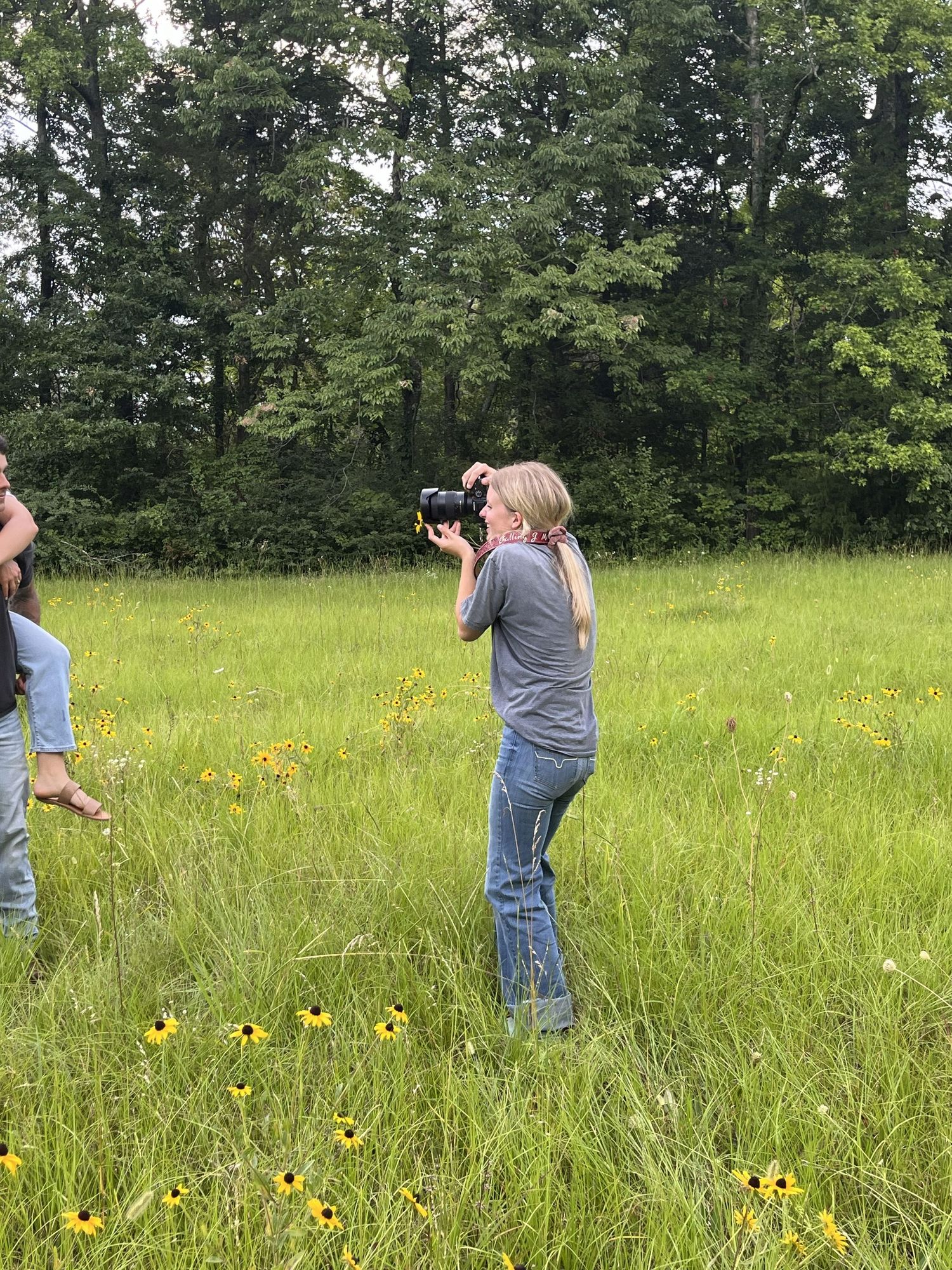 Behind-the-scenes photography of Joy Nabors capturing portraits during a photo session in a field.
