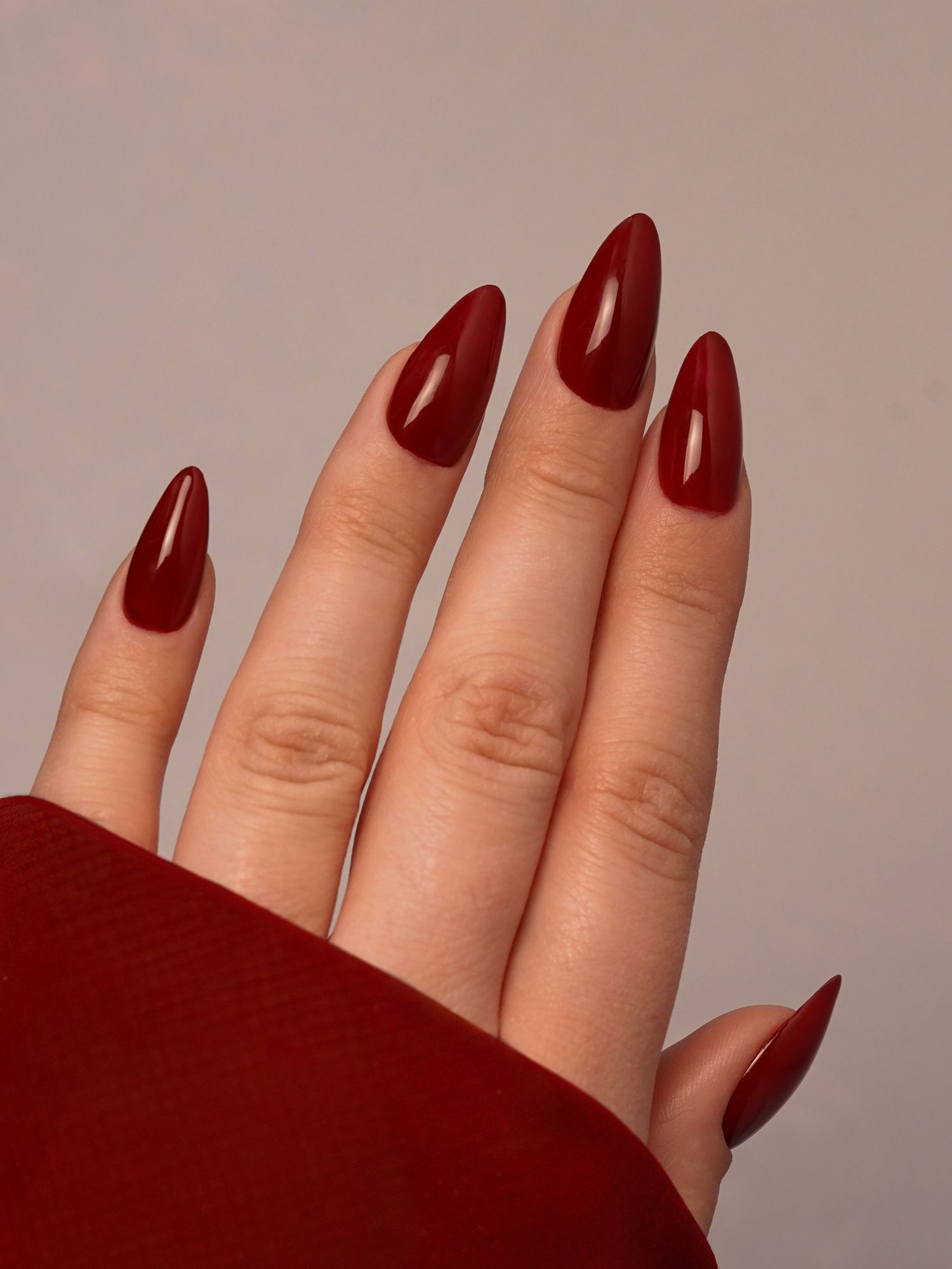 Glossy dark red stiletto nails on a hand against a neutral background.
