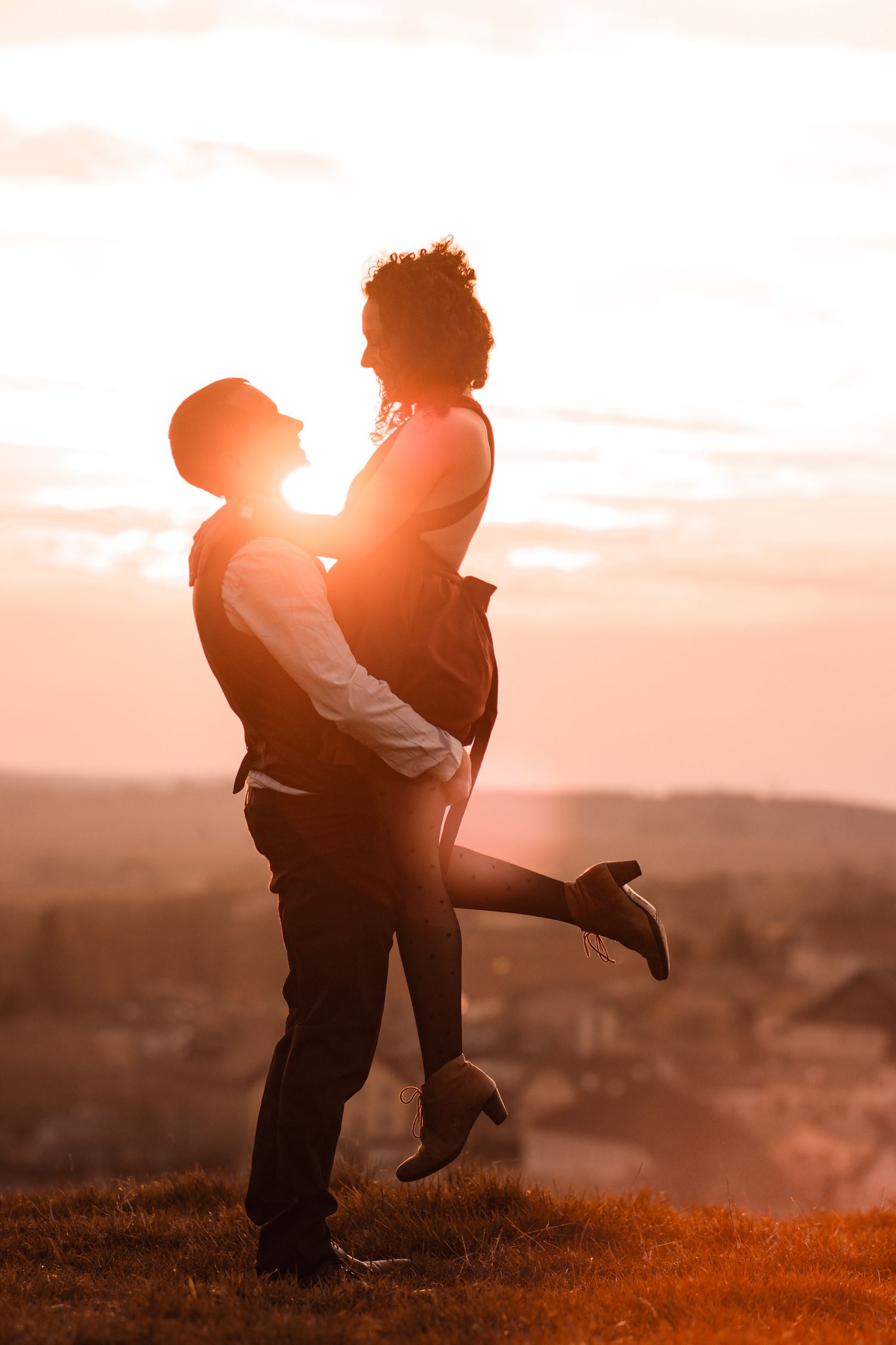 Man lifting woman in his arms against a stunning golden sunset skyline outdoors.
