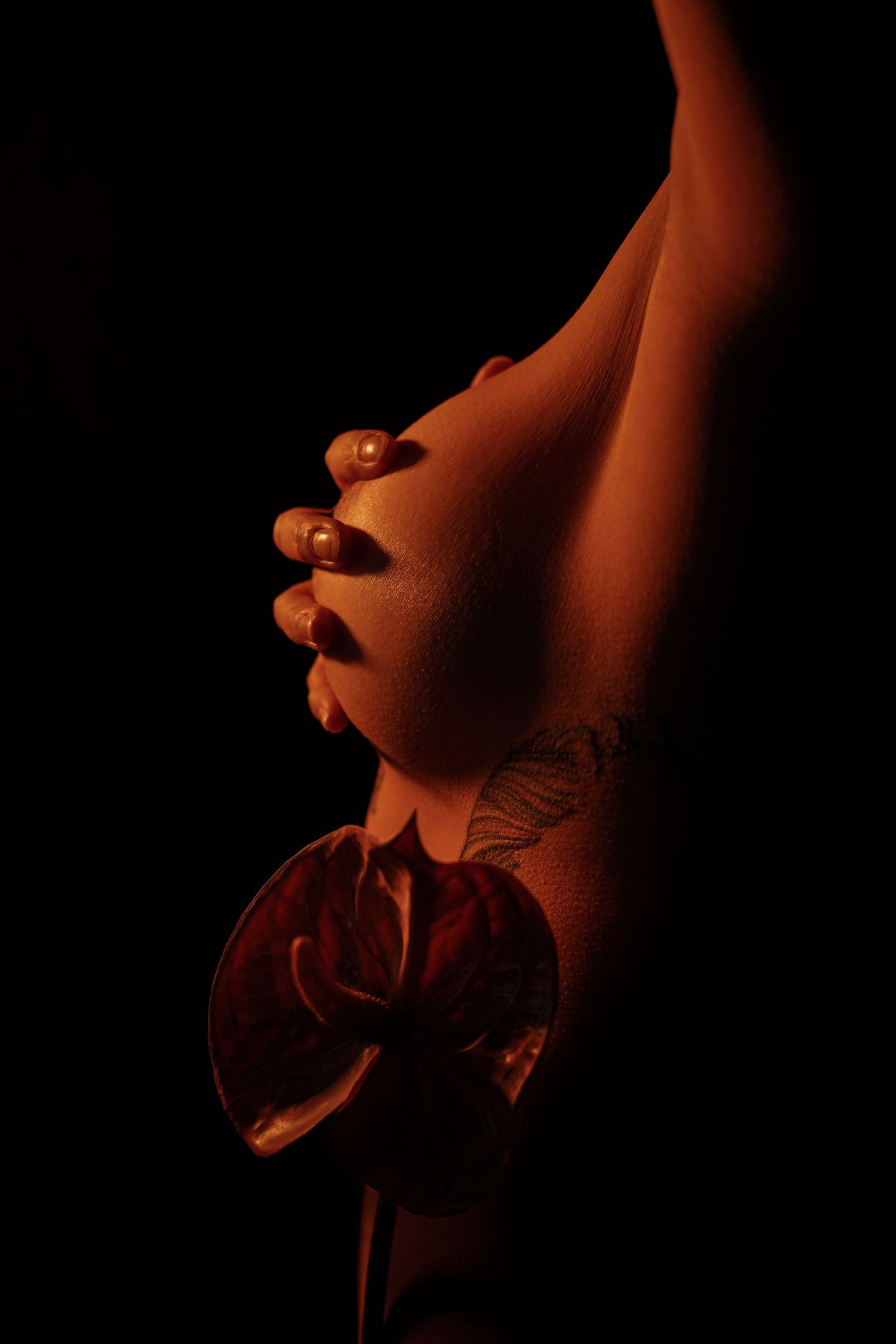 Close-up of a woman with a butterfly tattoo holding an anthurium flower in dramatic red lighting.
