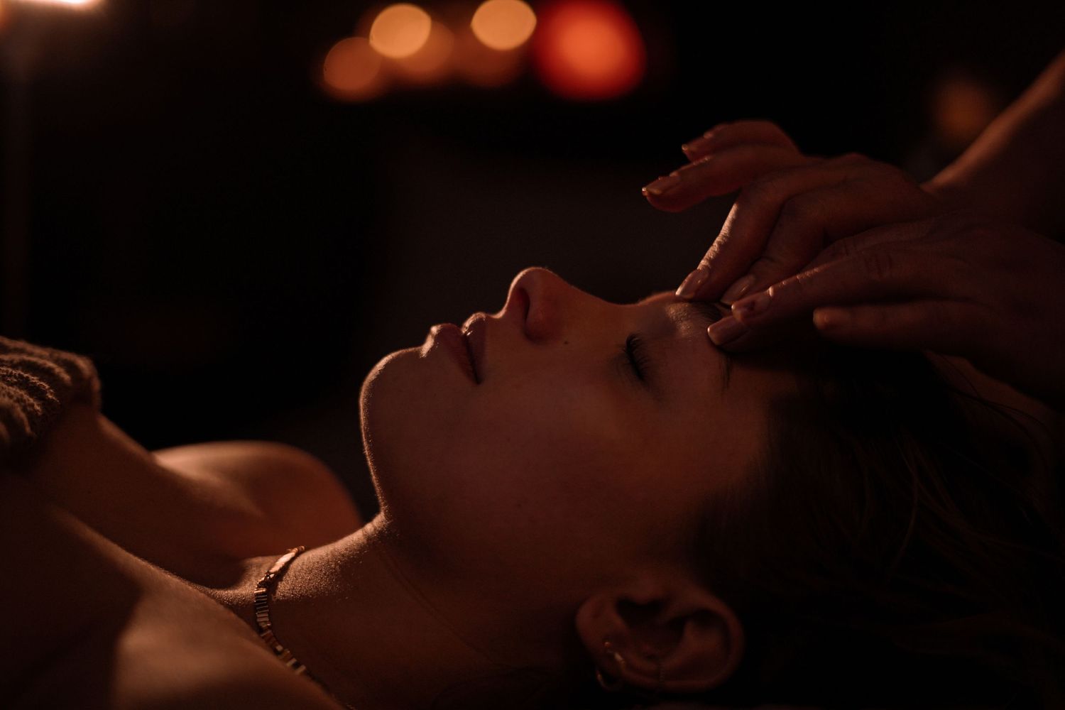 Close-up of a woman receiving a relaxing facial massage in a warm candlelit spa setting.
