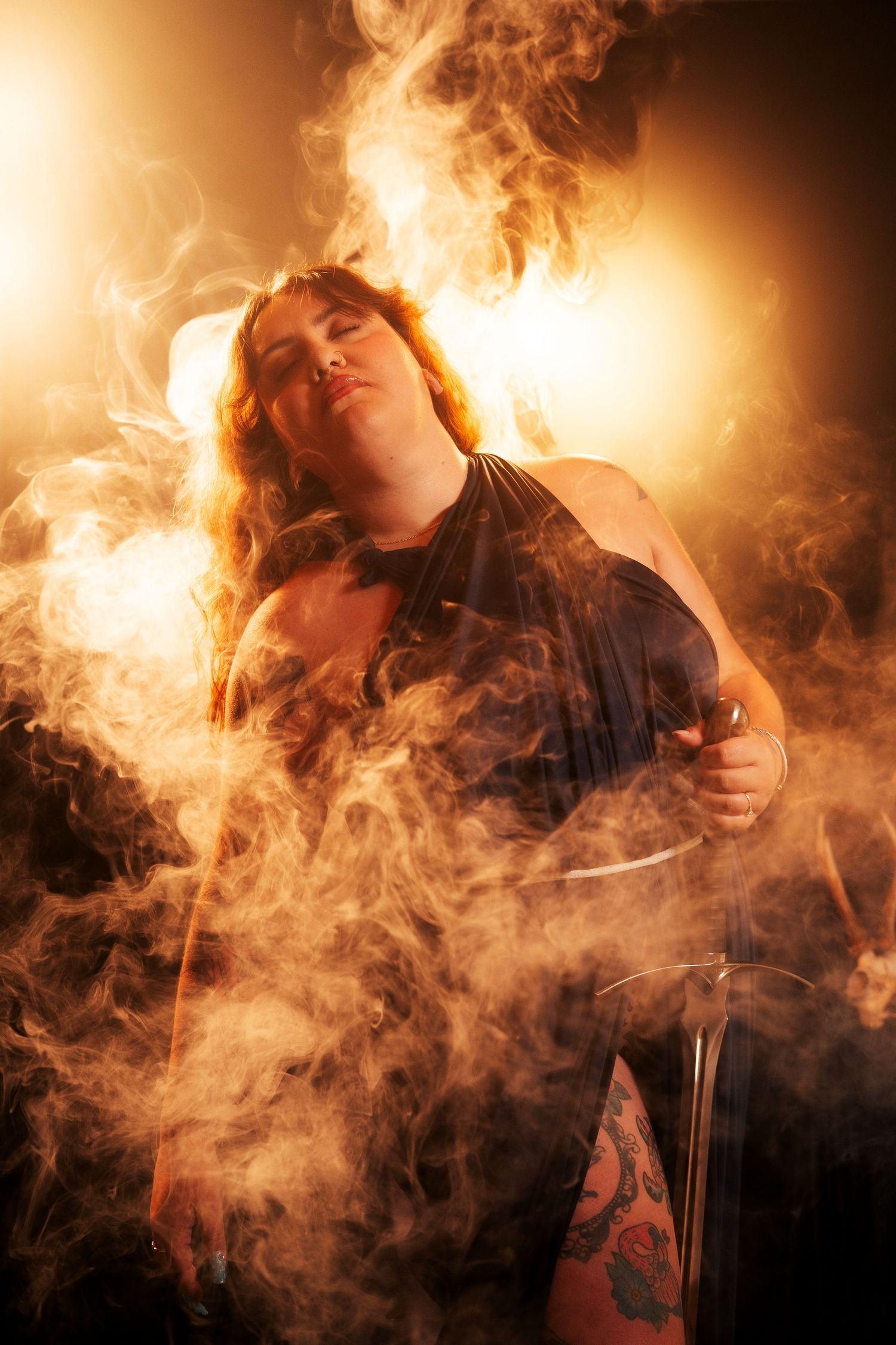 Woman in dark dress surrounded by dramatic smoke and golden stage lighting.