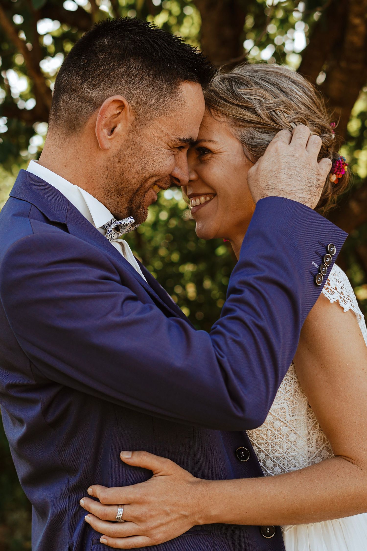 Smiling bride and groom in blue suit sharing joyful embrace outdoors on wedding day.
