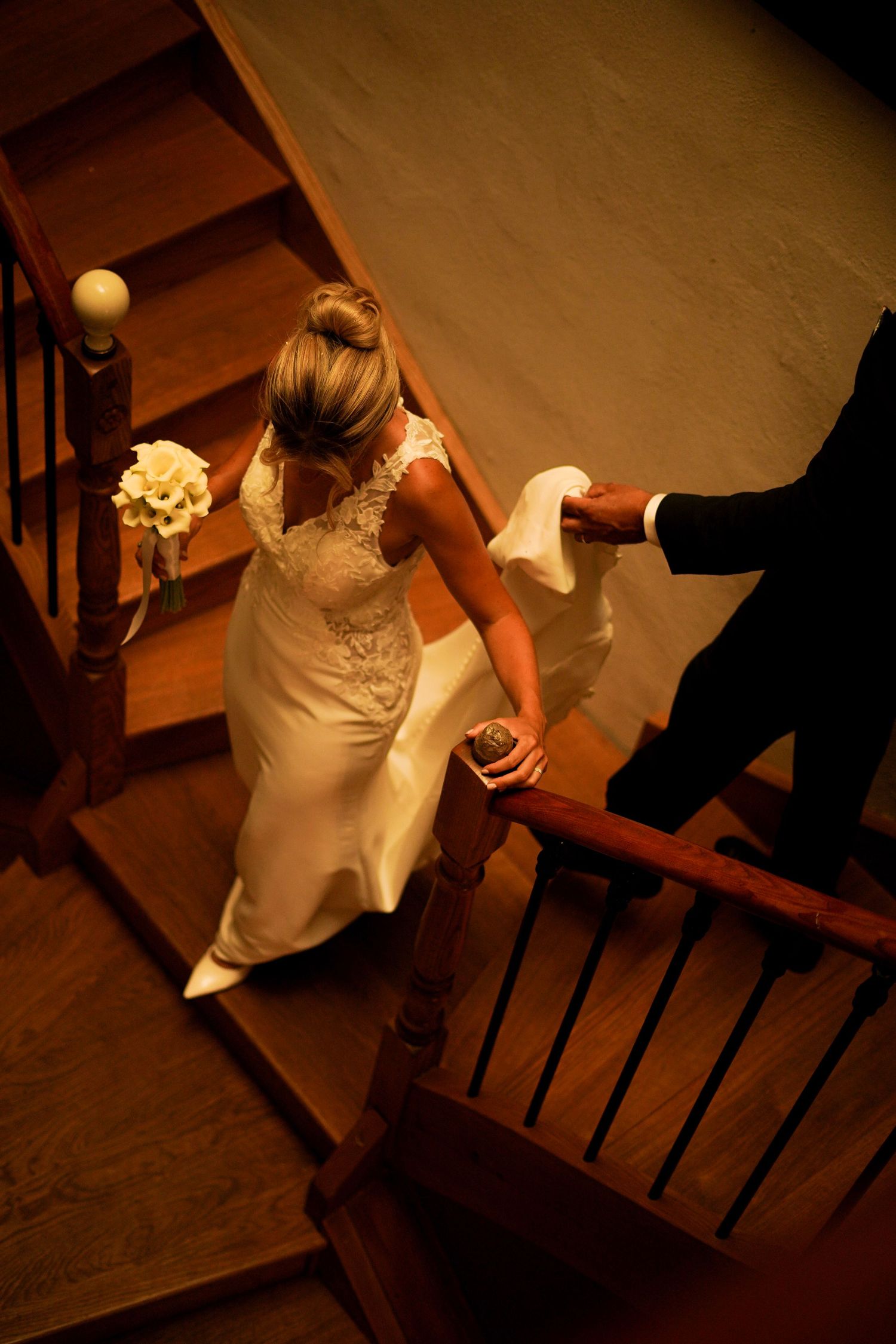 Aerial view of bride in lace wedding dress walking up wooden staircase with groom.