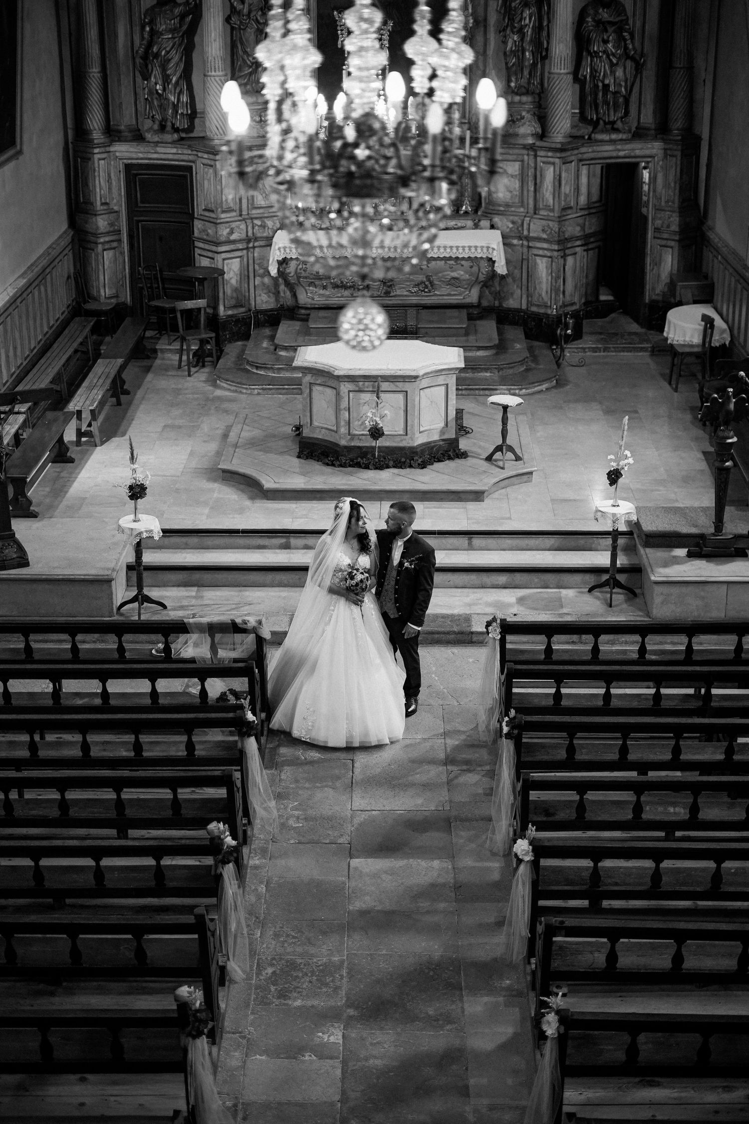 Black and white aerial view of bride and groom standing at the altar of an ornate church.